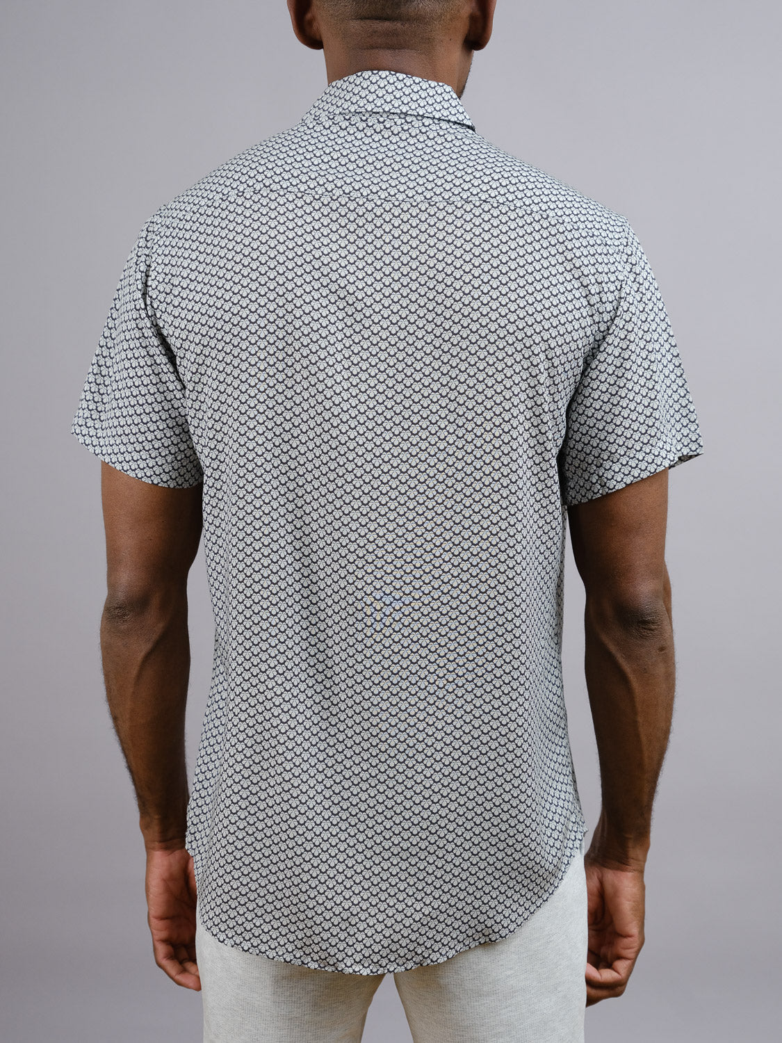 A person is seen from behind wearing the ID Menswear Toyo Japanese Print Shirt, a lightweight short-sleeve rayon shirt with vibrant prints, paired with light-colored pants against a plain gray background.