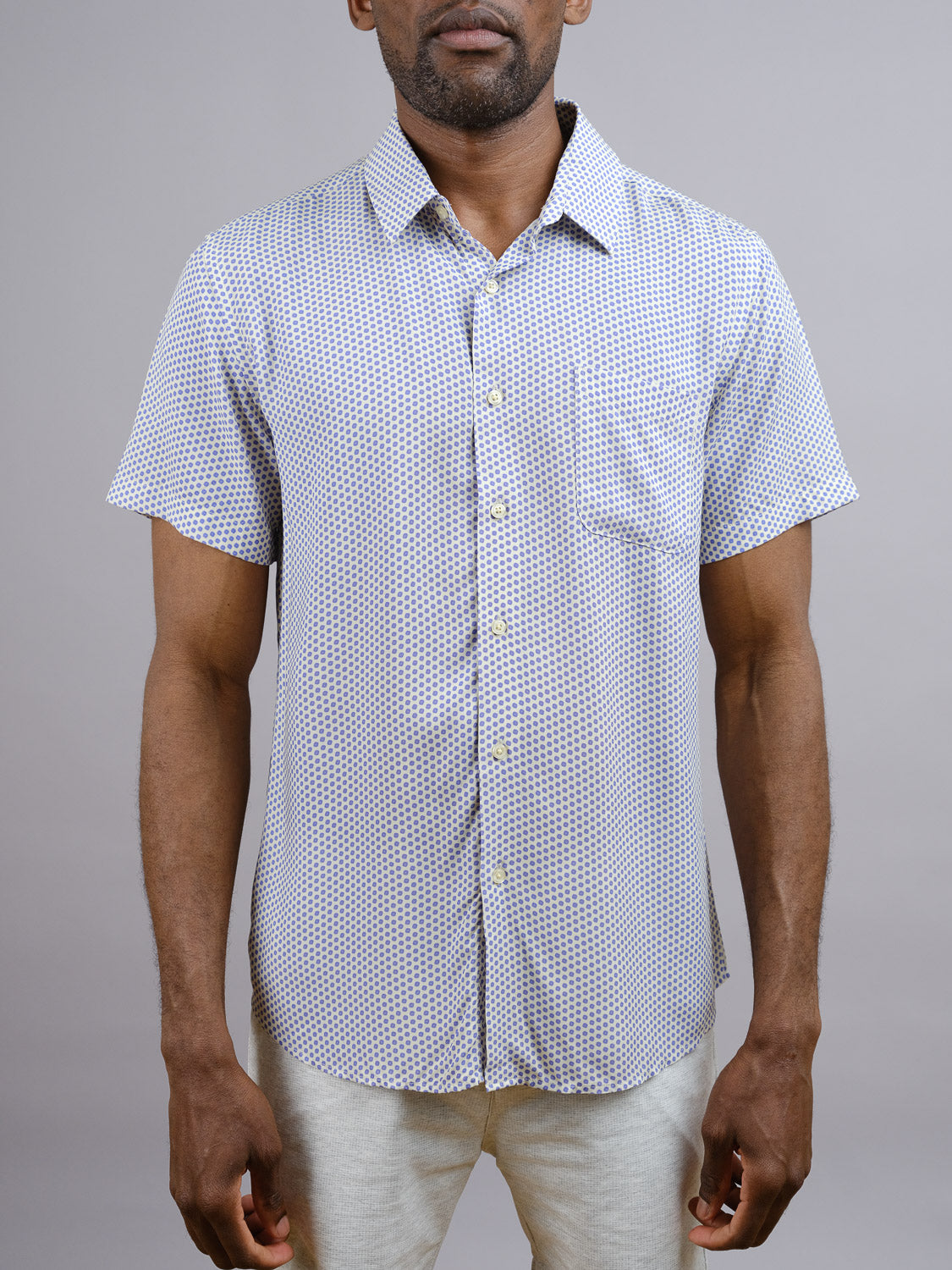 A man wears the Shibori Japanese Print Shirt by ID Menswear, a short-sleeve rayon shirt with a small geometric pattern and front pocket, ideal for warm weather, standing against a plain gray background.