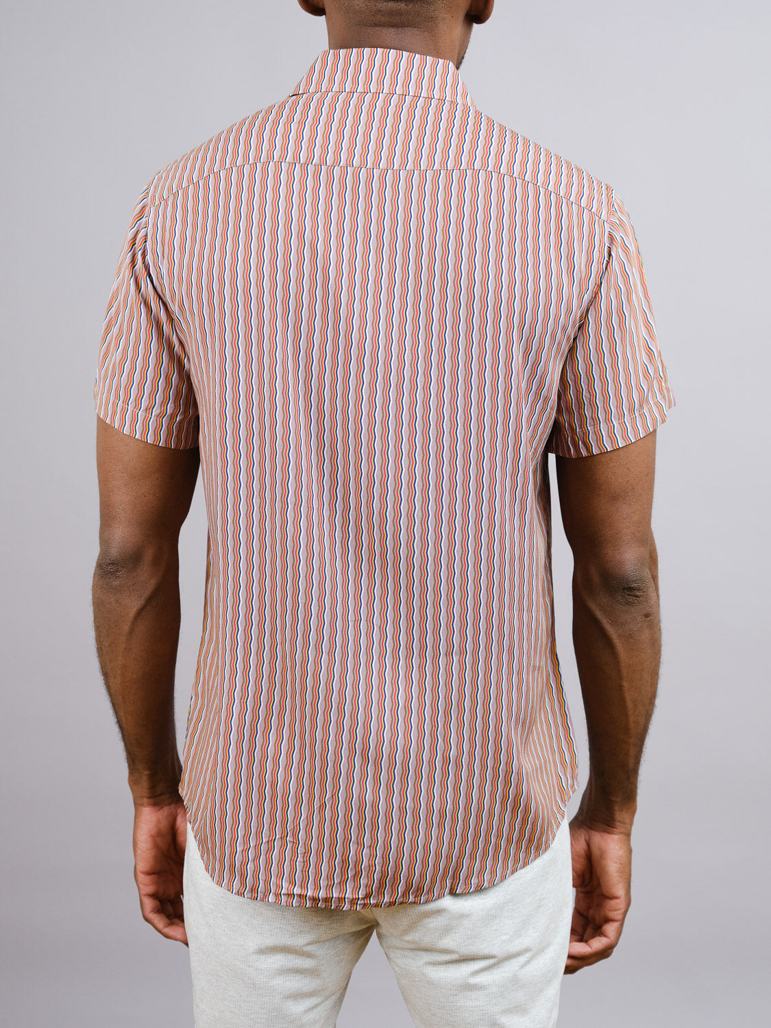 A person faces away from the camera in a Jigu Geometric Printed Shirt by ID Menswear—featuring vibrant vertical red, blue, and white stripes—paired with light pants against a plain light gray background; ideal for warm days.