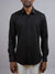 A man stands against a plain gray background wearing the ID Menswear Alex 4-Way Stretch Slim Dress Shirt in black with light-colored pants. His face is partially out of frame.