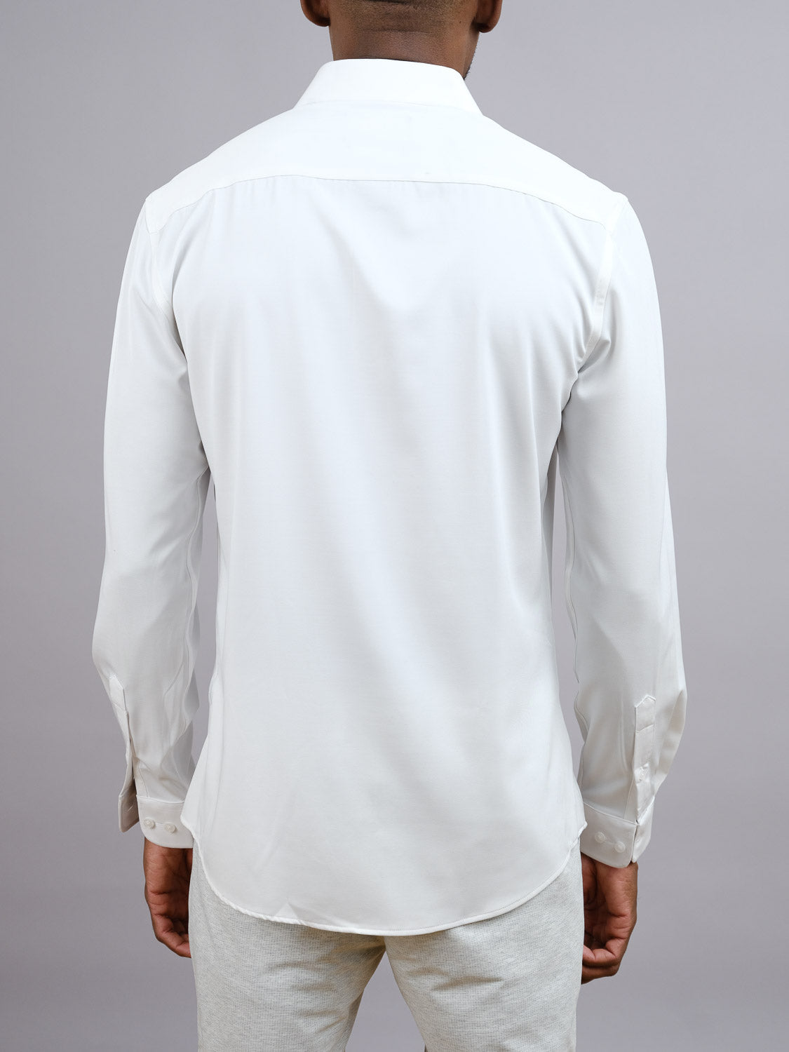 A man stands with his back to the camera, modeling the Alex 4-Way Stretch Slim Dress Shirt by ID Menswear and light-colored pants, set against a plain gray background.