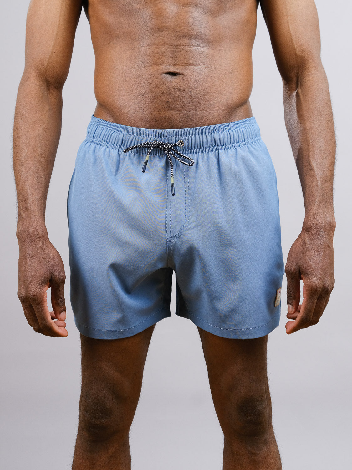 A person wears ID Menswears Oyogu Quick Dry 4 Way Stretch Swim Trunk in light blue, made from recycled plastic bottles, standing facing forward against a plain background with arms relaxed at their sides.