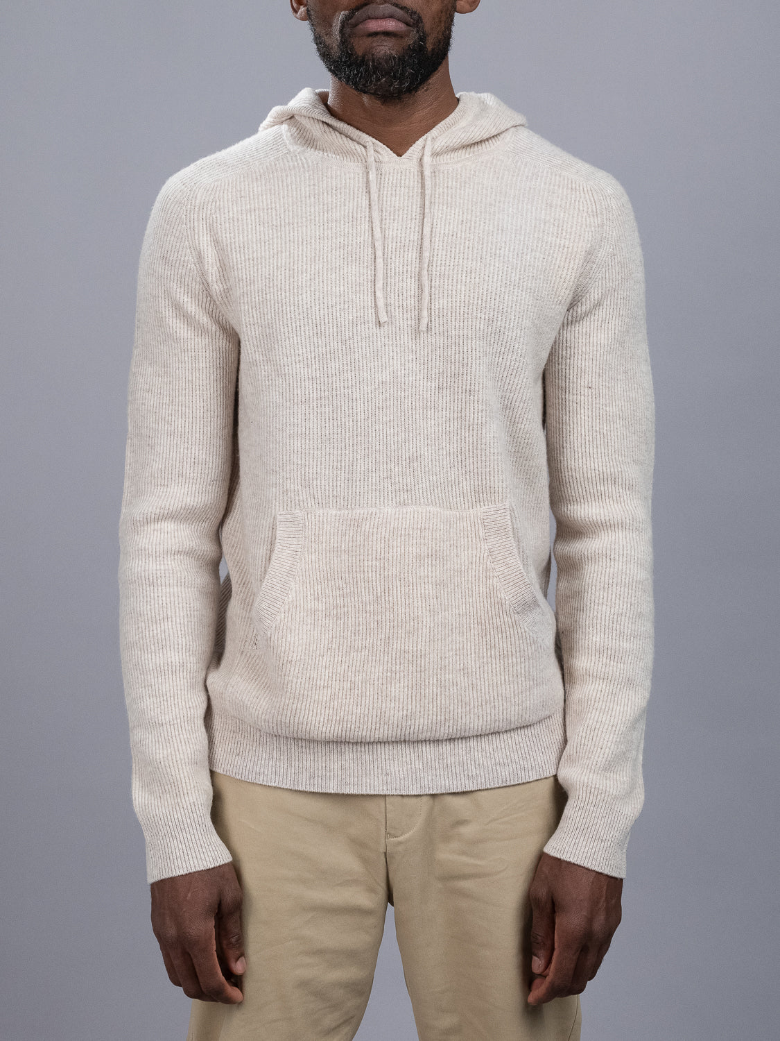 A man stands against a gray background, wearing khaki pants and the ID Menswear Skien Merino Wool Hoody, a luxurious knit with a front pocket—an essential for any cold-weather wardrobe.