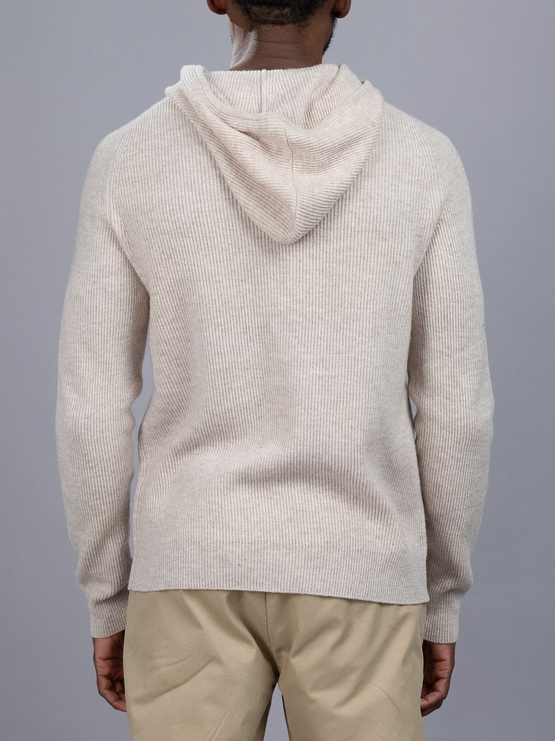 Someone is seen from behind wearing the Skien Merino Wool Hoody in light beige by ID Menswear with tan pants, standing before a plain gray background—an ideal choice for your cold-weather wardrobe.