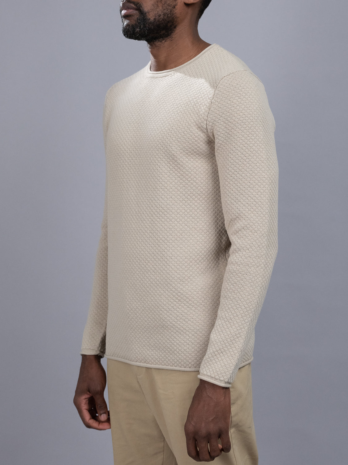 A person stands in profile against a gray background, wearing a Westside Rolled Crew Neck Sweater from ID Menswear and khaki pants.