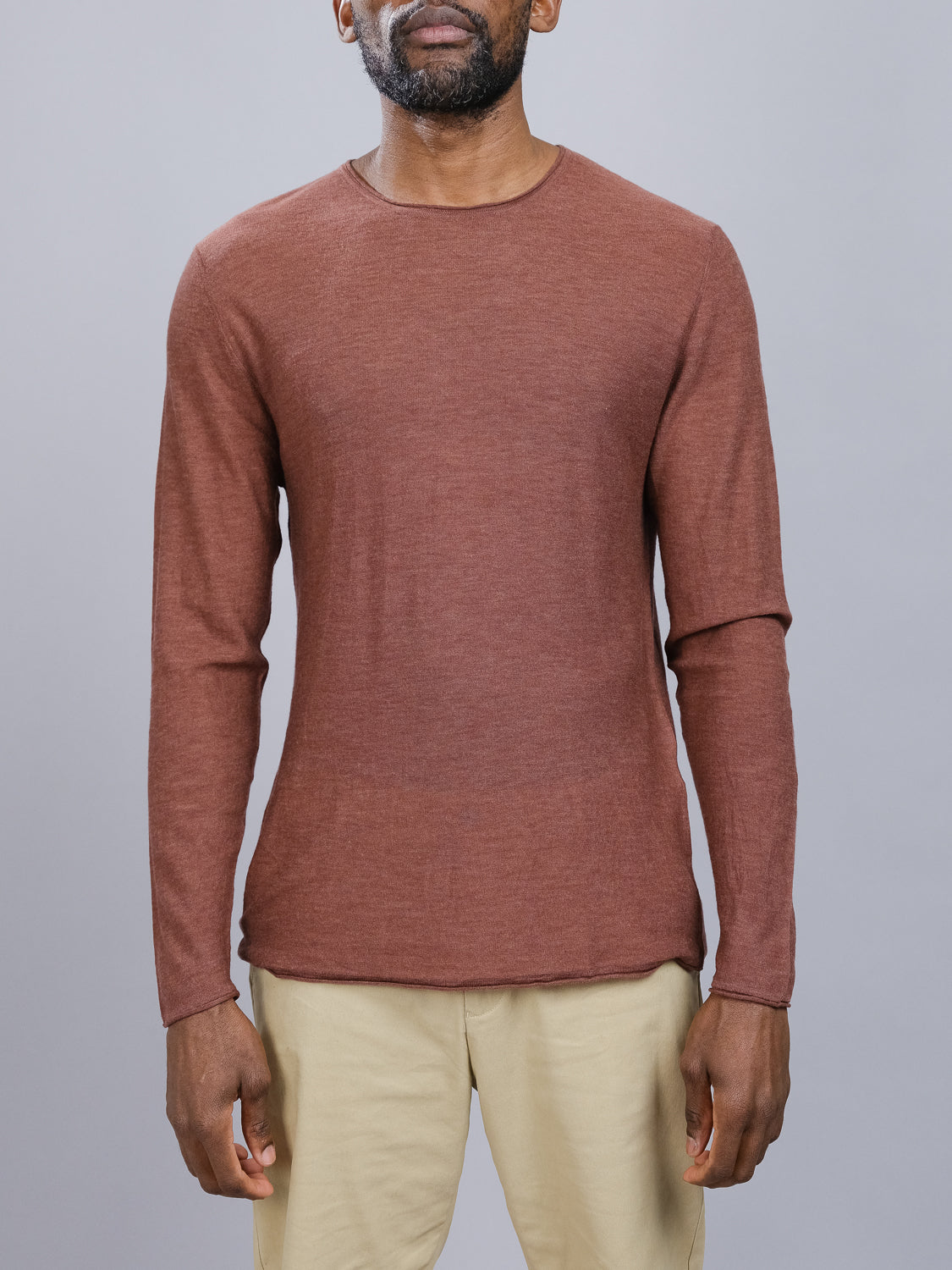A man in an ID Menswear Vogue Lightweight Merino Sweater, featuring long sleeves in brown, pairs it with beige pants against a plain gray background, showing only his upper body.