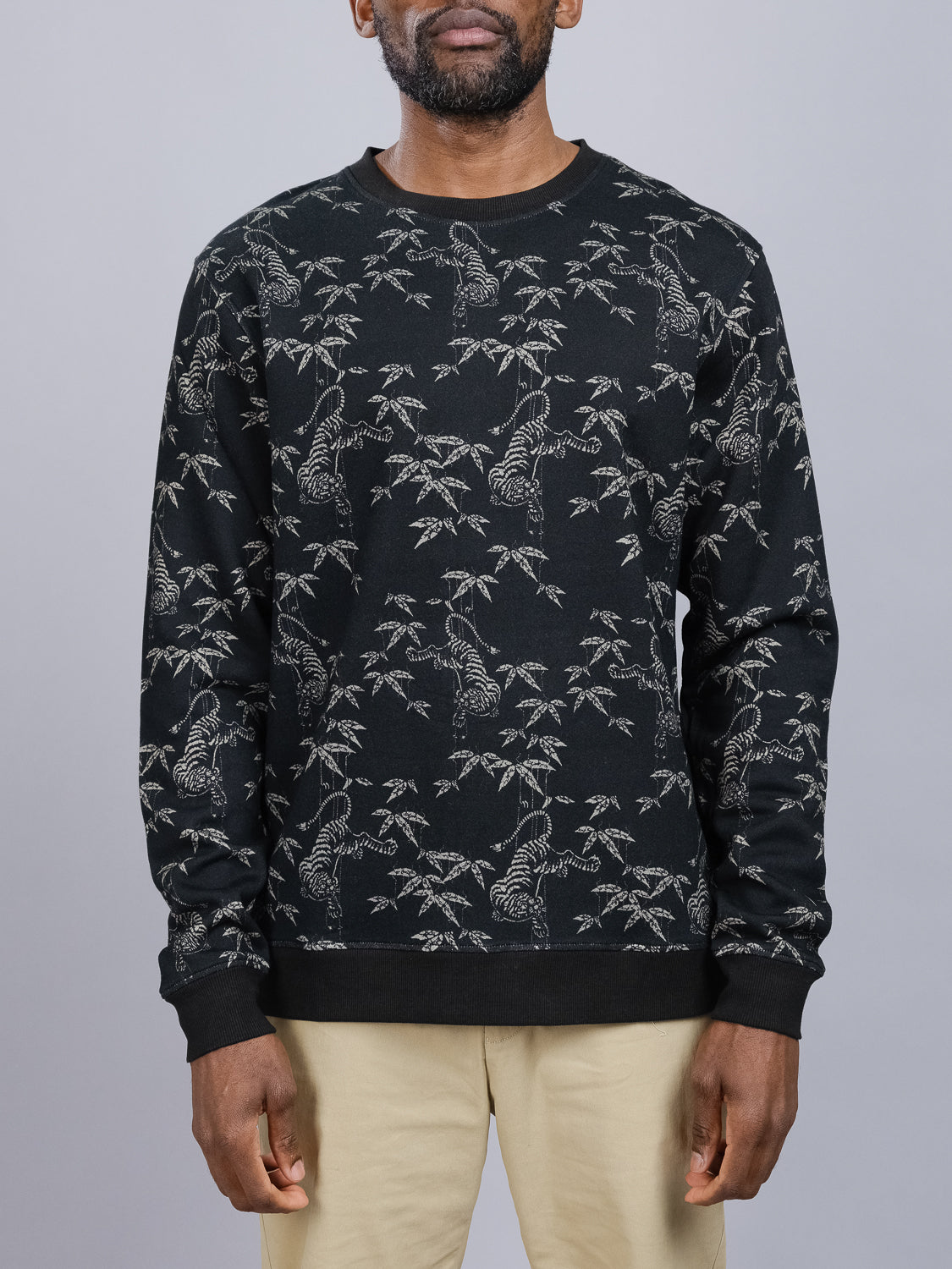 A man wearing the ID Menswear Tiger Bamboo Printed Sweatshirt featuring a white tiger and bamboo design, paired with beige pants against a plain gray background.