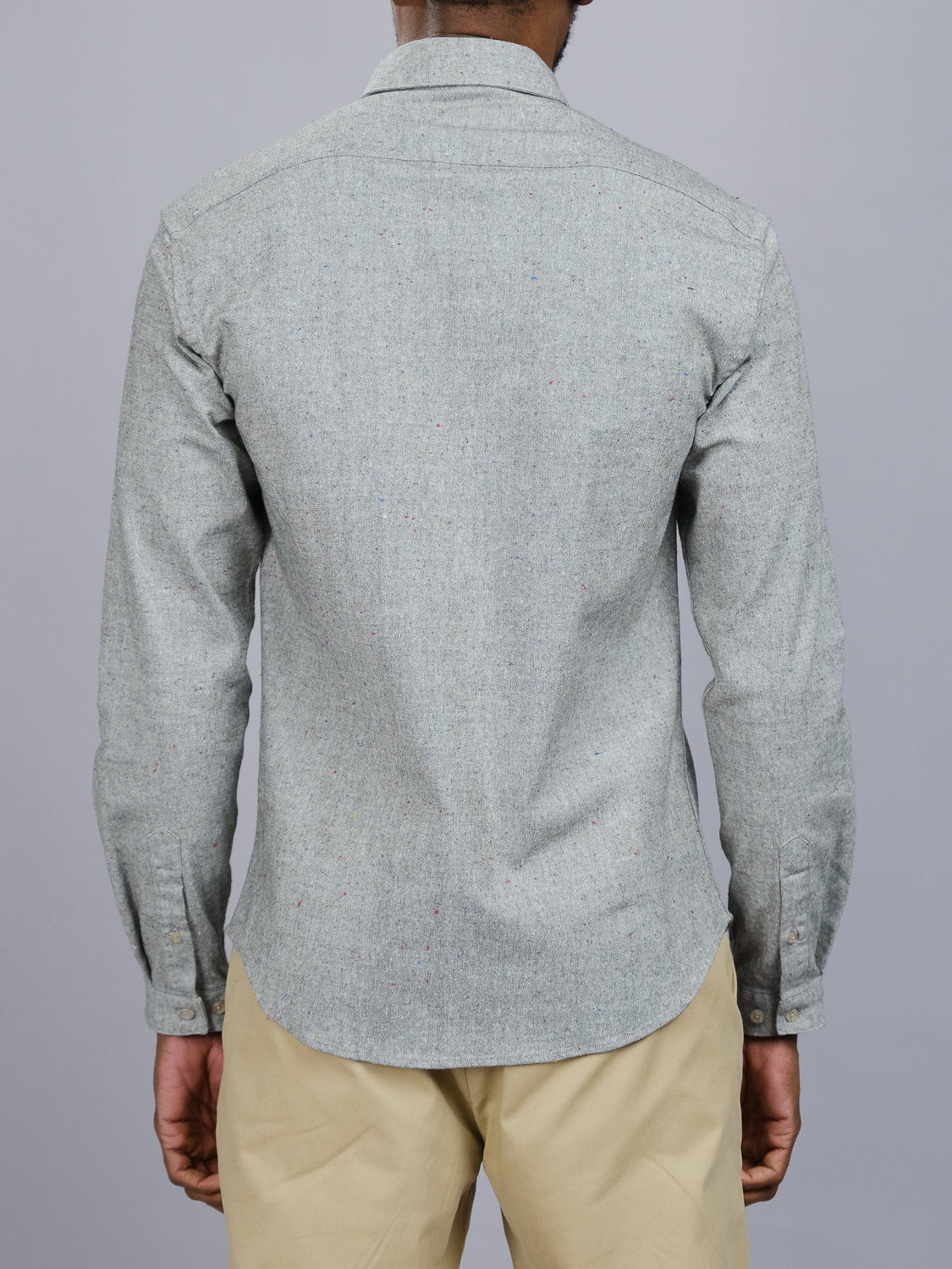Rear view of a person wearing the ID Menswear Allswell Speckled Button Down Shirt in a premium cotton-linen blend, long-sleeved, paired with beige pants against a gray background.