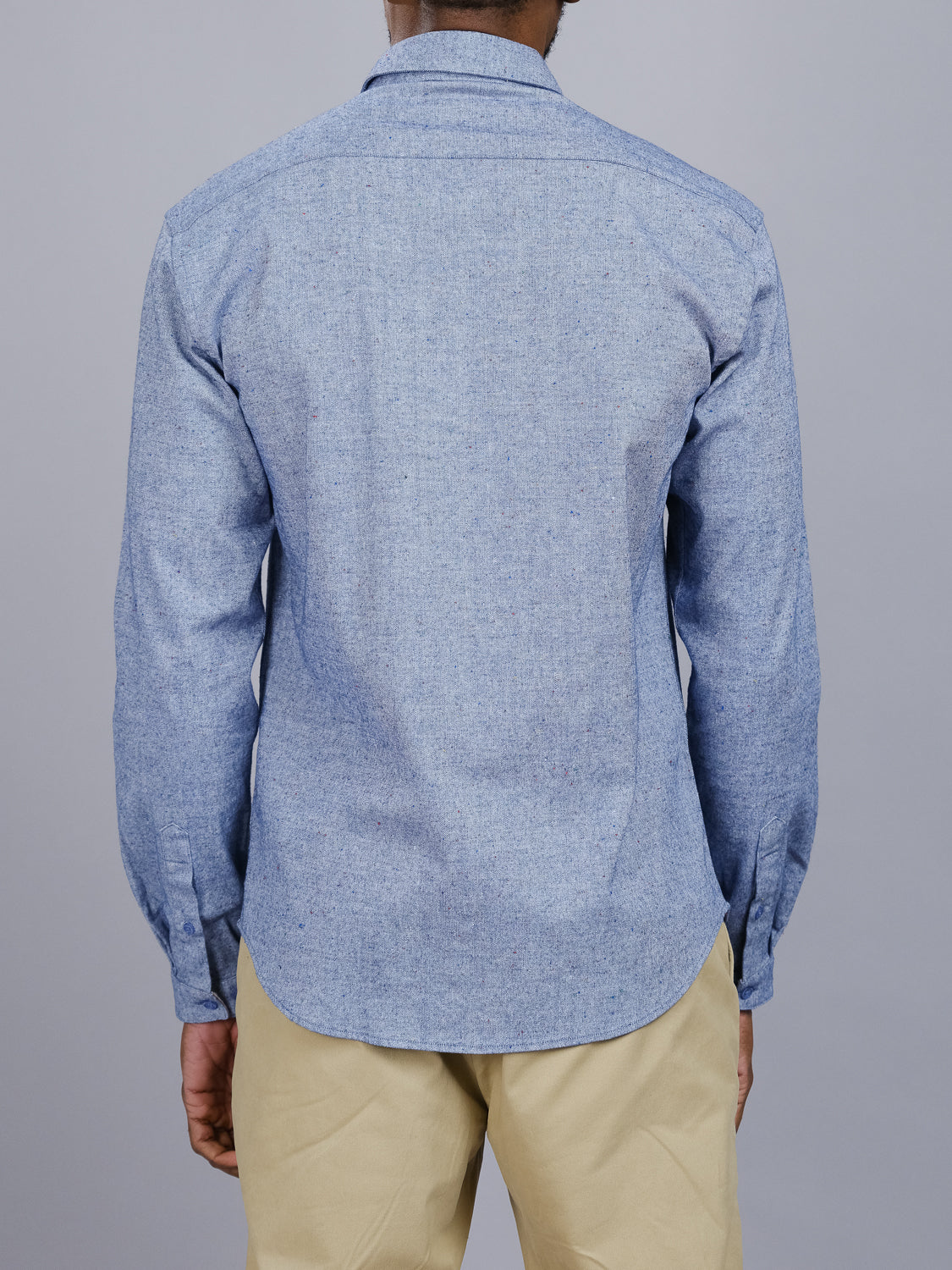 Dressed in an Allswell Speckled Button Down Shirt by ID Menswear, made from a premium cotton-linen blend, the individual perfectly pairs it with beige pants against a plain gray background.