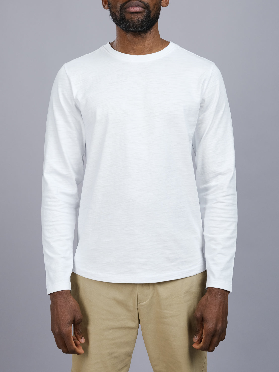 Person models ID Menswears Paradise Long Sleeve Tee with beige pants against a gray background, highlighting the upper body and sleeves.