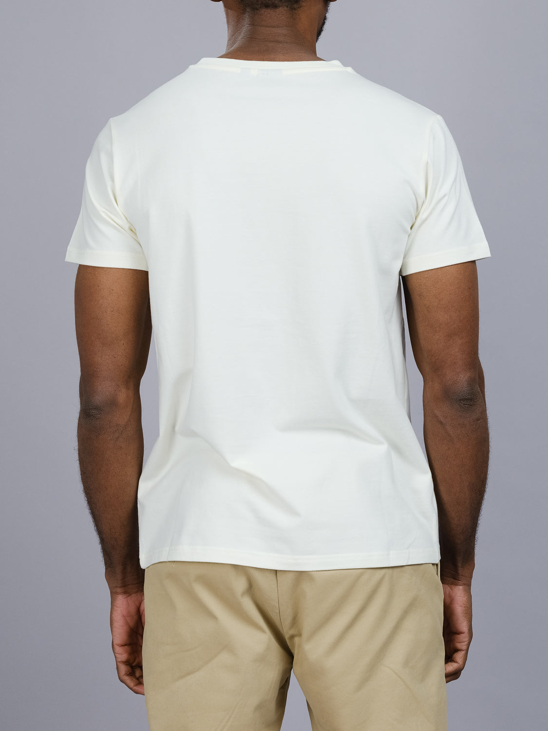 Photographed from behind against a gray backdrop, a man wears the ID Menswear Classic V Neck Tee with beige pants. This wardrobe staple, made from a comfy cotton-spandex blend, provides style and comfort for any occasion.