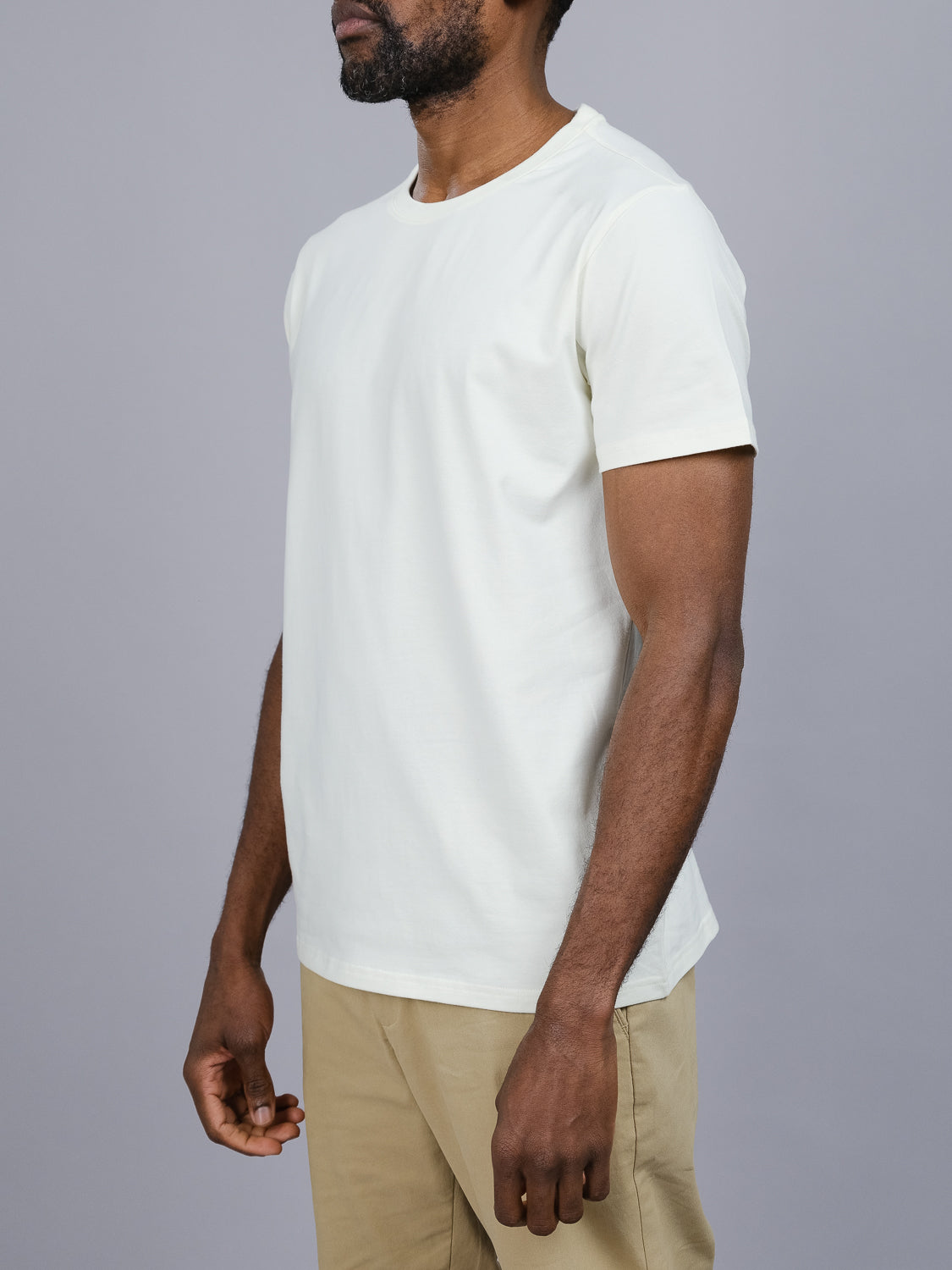 In ID Menswears regular fit Classic Crew Neck Tee and beige pants, a person stands against a gray backdrop. Shown from the shoulders down with their head partially out of frame, their relaxed arms emphasize the comfort of the cotton-spandex fabric.