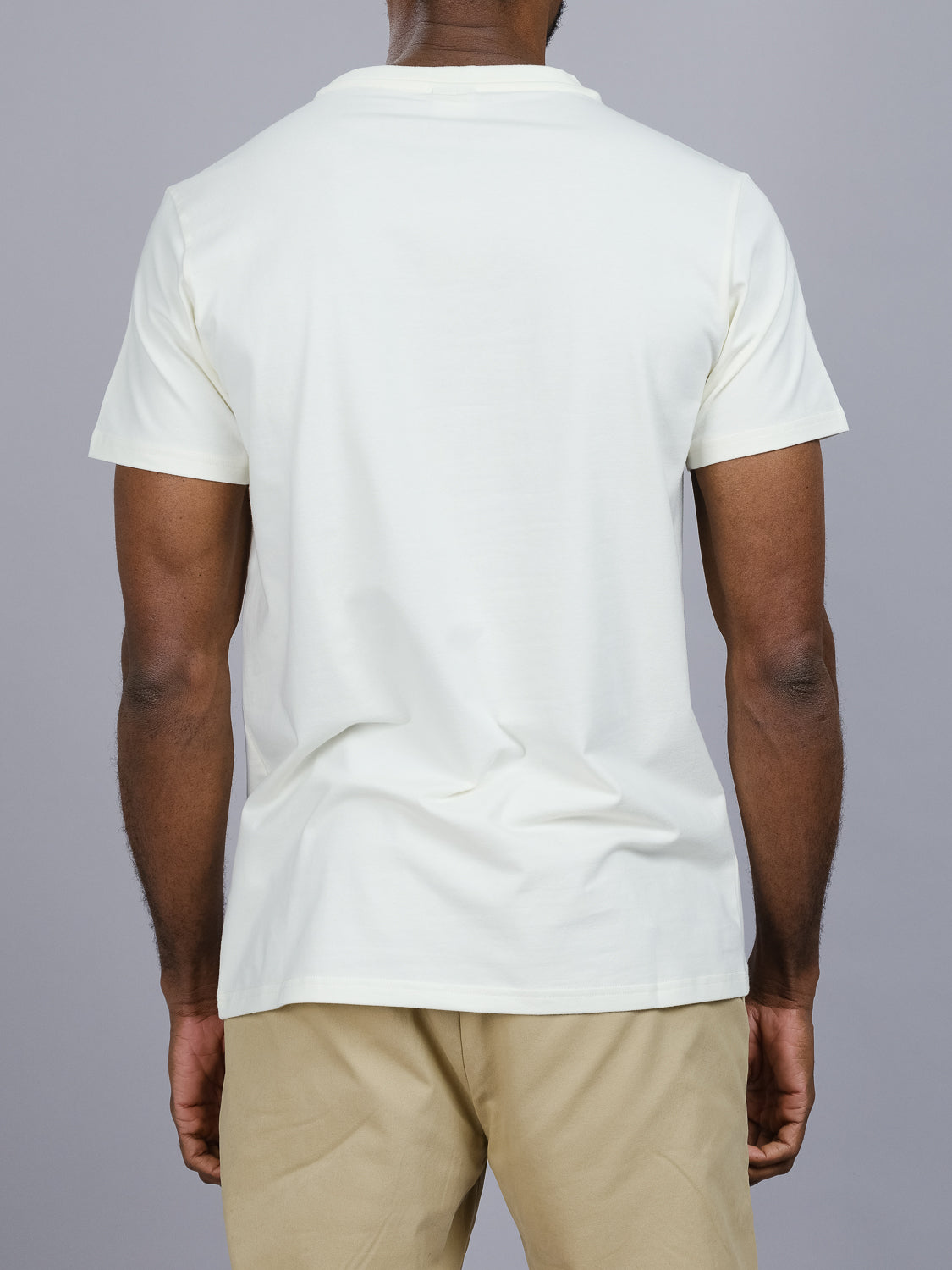 A person in an ID Menswear Classic Crew Neck Tee, light-colored, and beige pants stands with their back to a gray background, highlighting its regular fit that blends comfort and style.