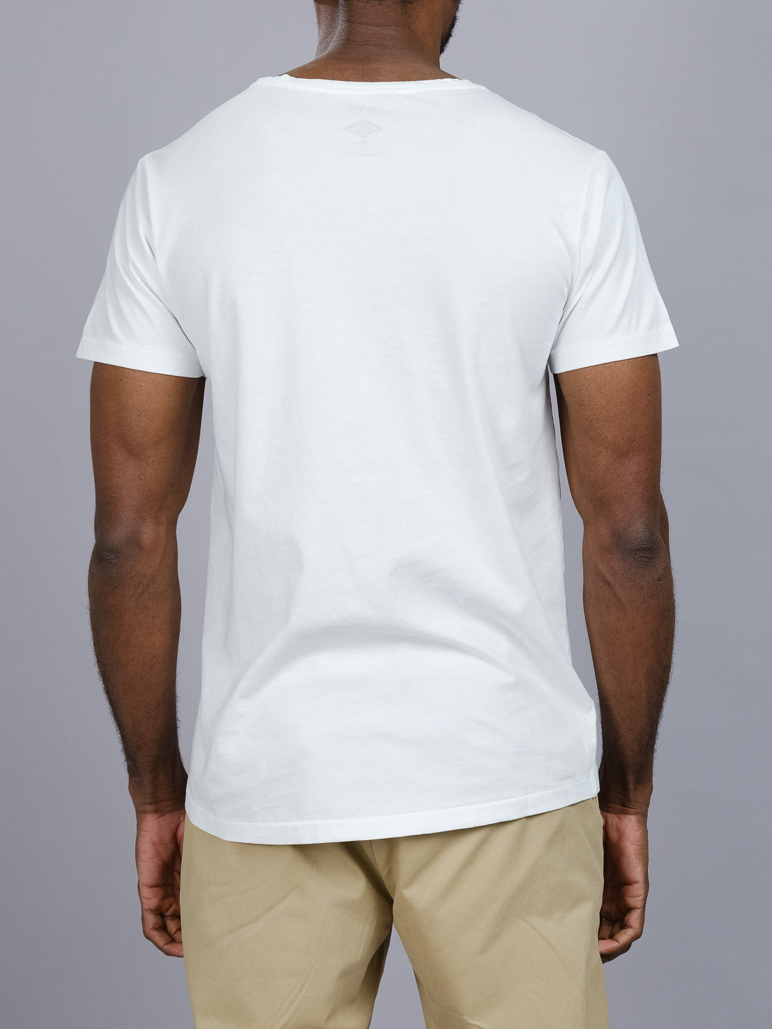 A person wearing a Legacy Organic Cotton V Neck Tee from ID Menswear and beige pants, viewed from the back against a gray background.
