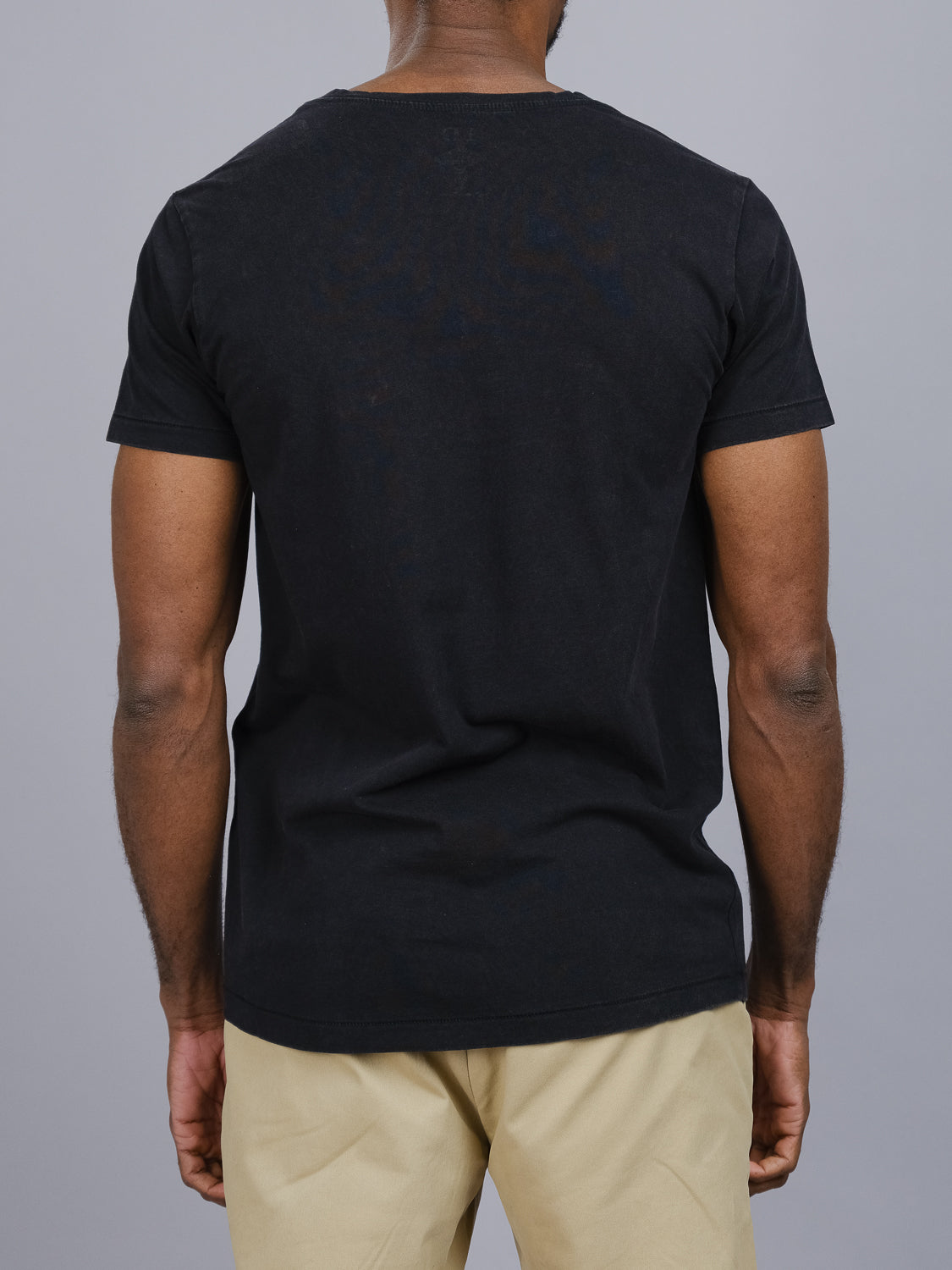 In front of a solid gray background, a person wears ID Menswears Legacy Organic Cotton V Neck Tee, pairing it with beige pants. This plain black classic fit T-shirt perfectly complements the understated vintage look.