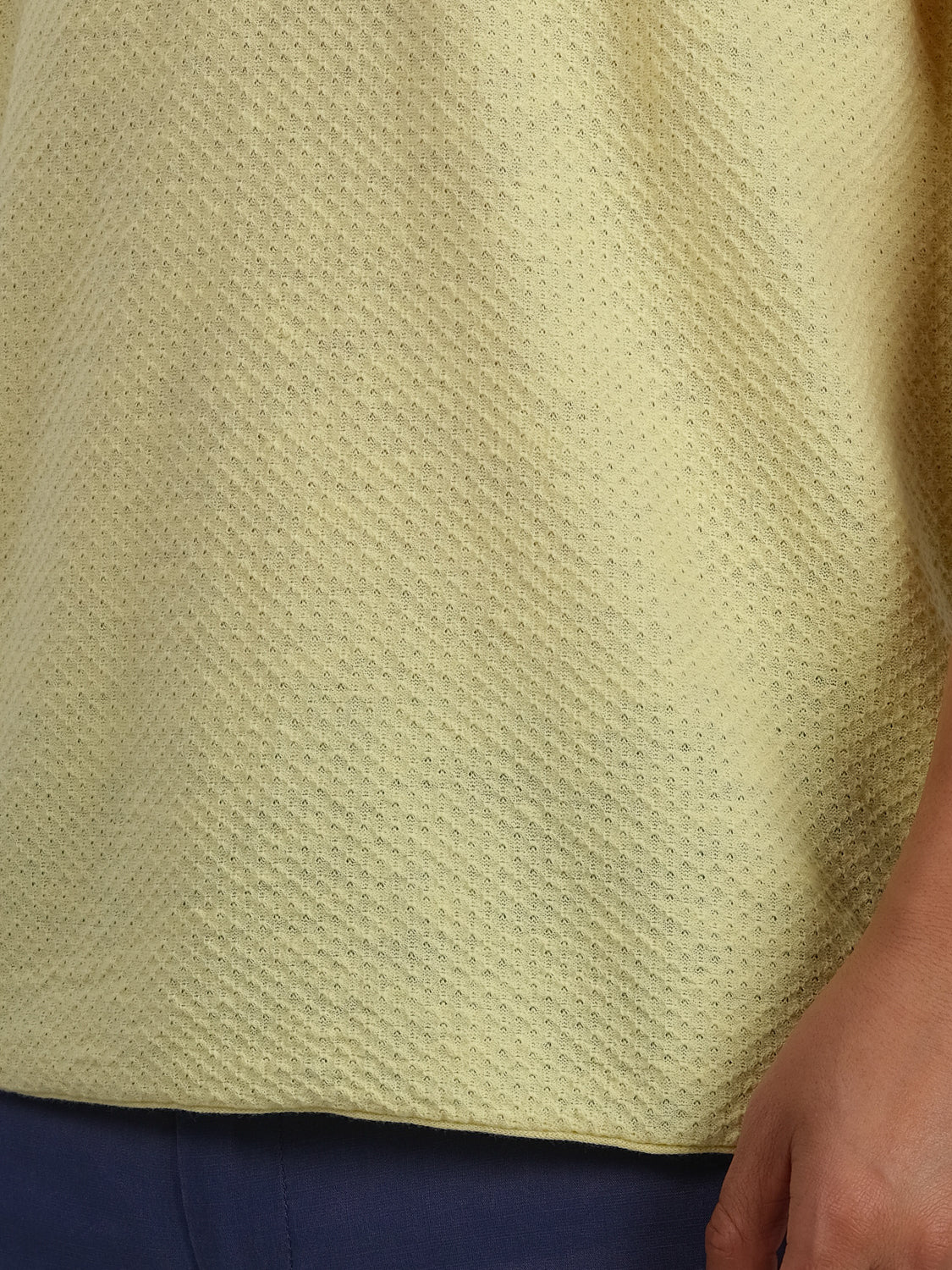 A person is wearing a light yellow Phoenix Super Fine Cotton Knit Polo from ID Menswear paired with dark blue pants, offering a versatile and stylish look. Their right hand rests casually by their side. The polo features a subtle dotted pattern, ideal for casual wear.