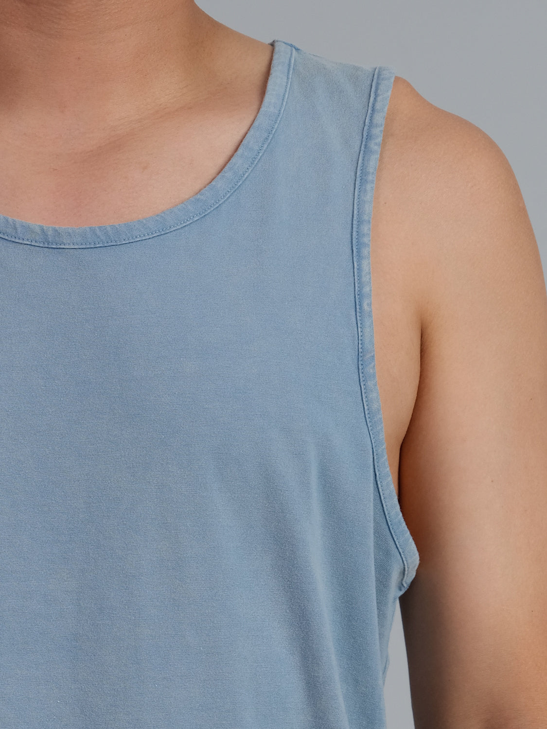 Against a plain gray background, an individual dons the ID Menswear Settler Snow Vintage Wash Tank Top, showcasing the lightweight texture and light blue hue of its organic cotton that lends a subtle vintage appearance.