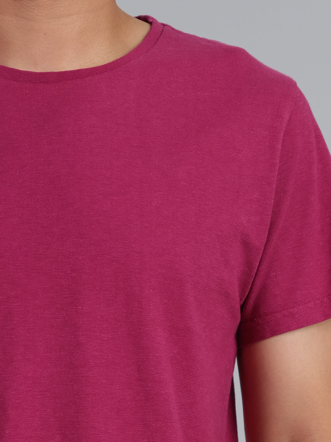 A person wears the Dope Hemp Organic Cotton Tee from ID Menswear, in magenta, crafted from a hemp cotton blend. The image highlights its sustainable, soft, slightly textured fabric from shoulder to neck against a neutral gray background.