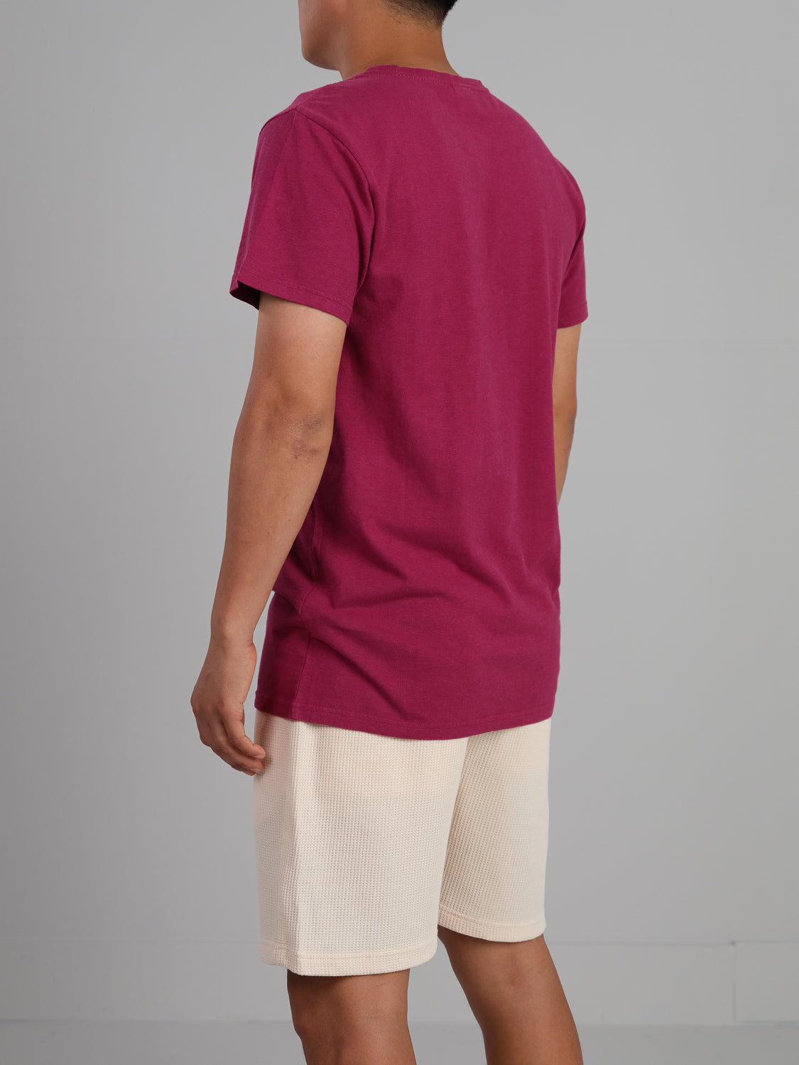 A person faces away wearing a maroon Dope Hemp Organic Cotton Tee by ID Menswear, paired with beige shorts. The plain gray background emphasizes the contrast of this casual, eco-friendly look.