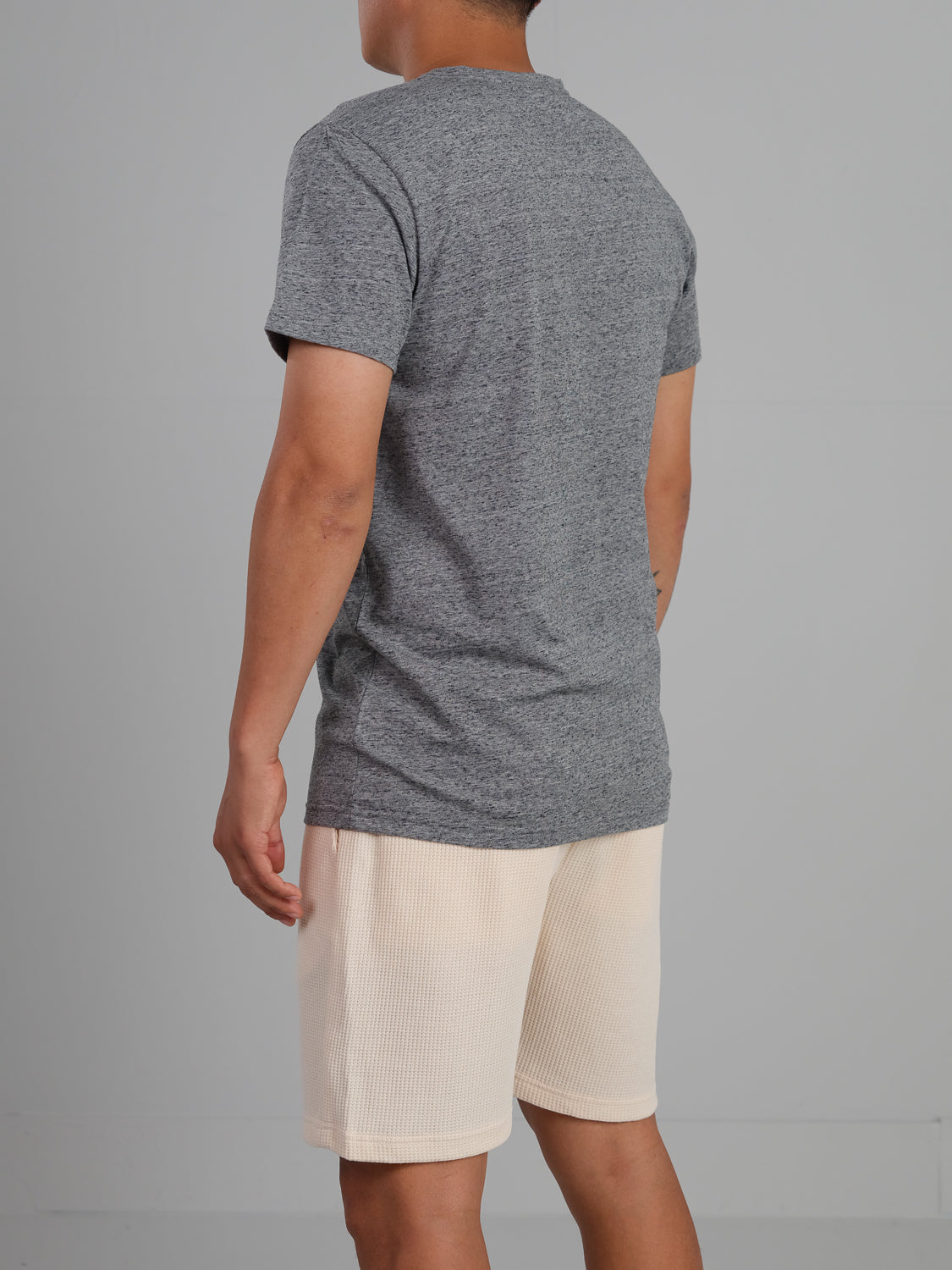 A person wears the Outclass Speckled Crew Neck Tee from ID Menswear, paired with light shorts. Designed for everyday comfort, its crafted from cozy cotton/poly jersey. They stand casually against a plain background with arms relaxed by their sides.