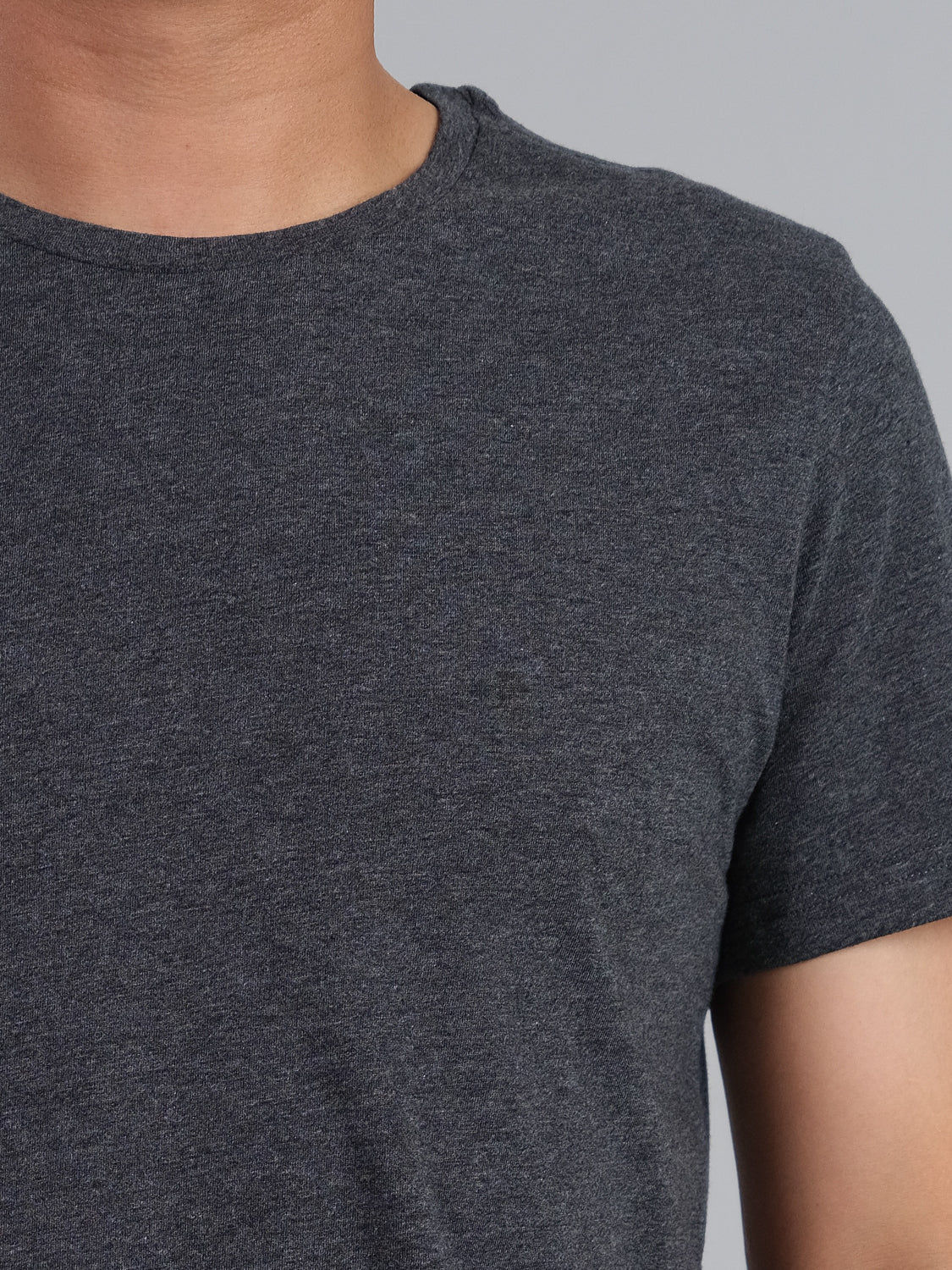 Close-up of a person in an ID Menswear Outclass Cotton Crew Neck Tee, dark gray with short sleeves, set against a neutral backdrop. The lightweight cotton jersey material gracefully contours their chest, shoulder, and neck.