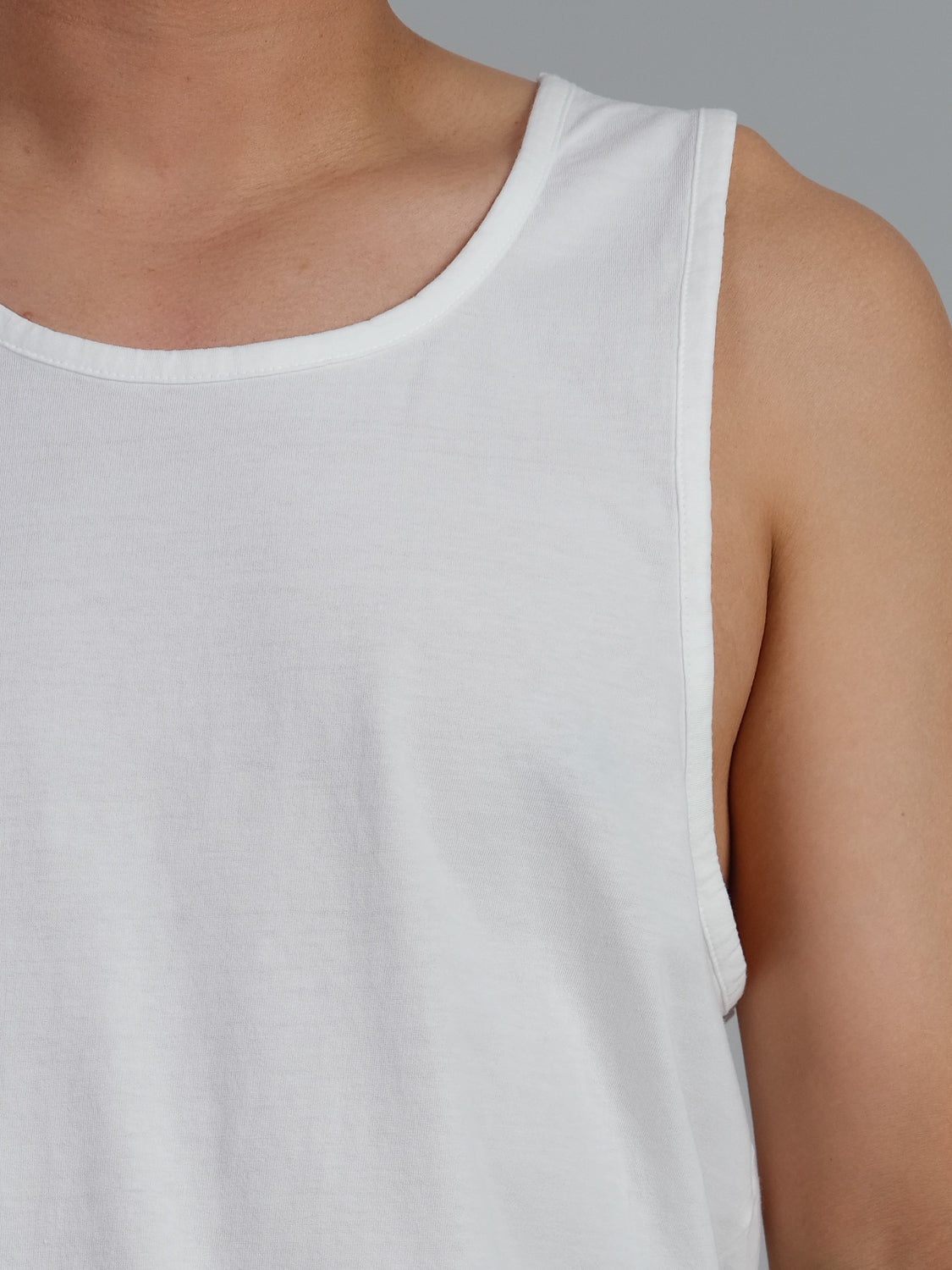 A close-up of someone wearing the Settler Organic Cotton Tank Top by ID Menswear. The focus is on the shoulder and upper chest against a gray background.