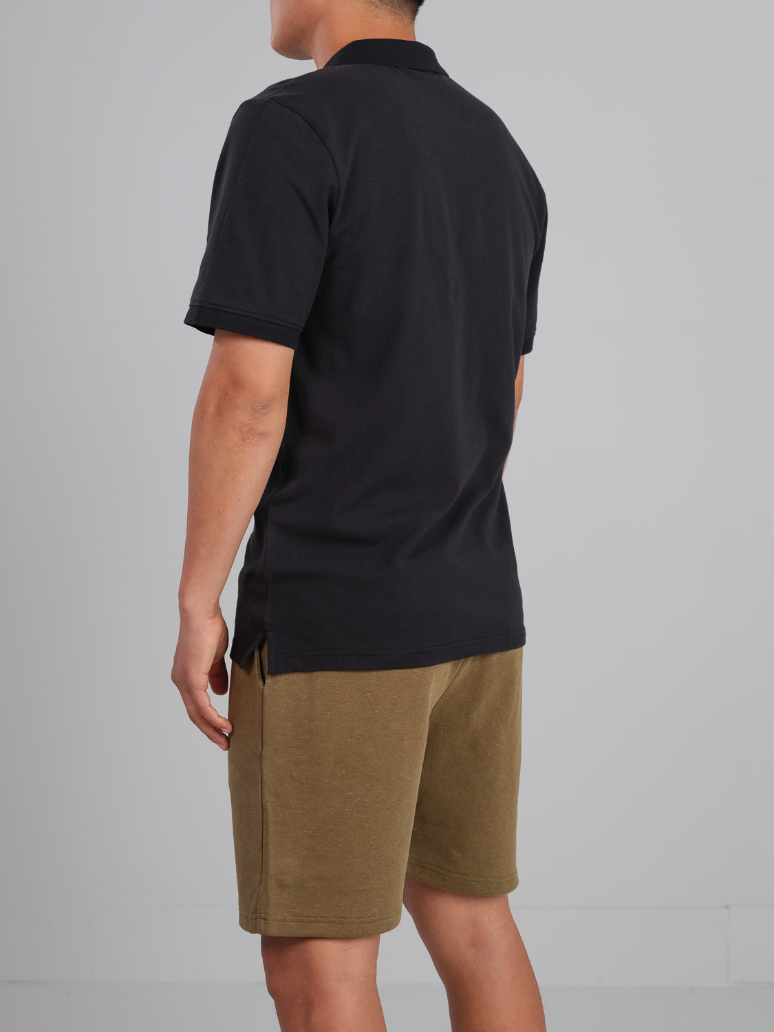 A person is standing with their back to the camera wearing an ID Menswear Ranger Classic Cotton Mesh Polo and olive green shorts against a plain, light-colored background.