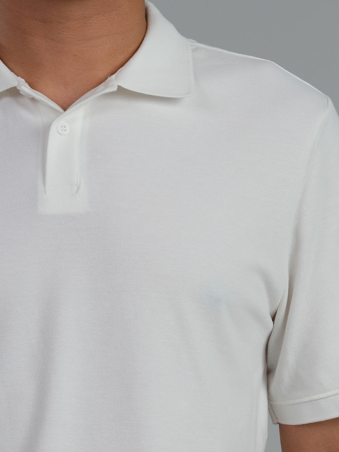 A close-up of a person wearing the Ranger Classic Cotton Mesh Polo by ID Menswear, highlighting its timeless style. The lightweight white shirt has a classic collar and buttons set against a gray background, showcasing its simple design on the upper torso.