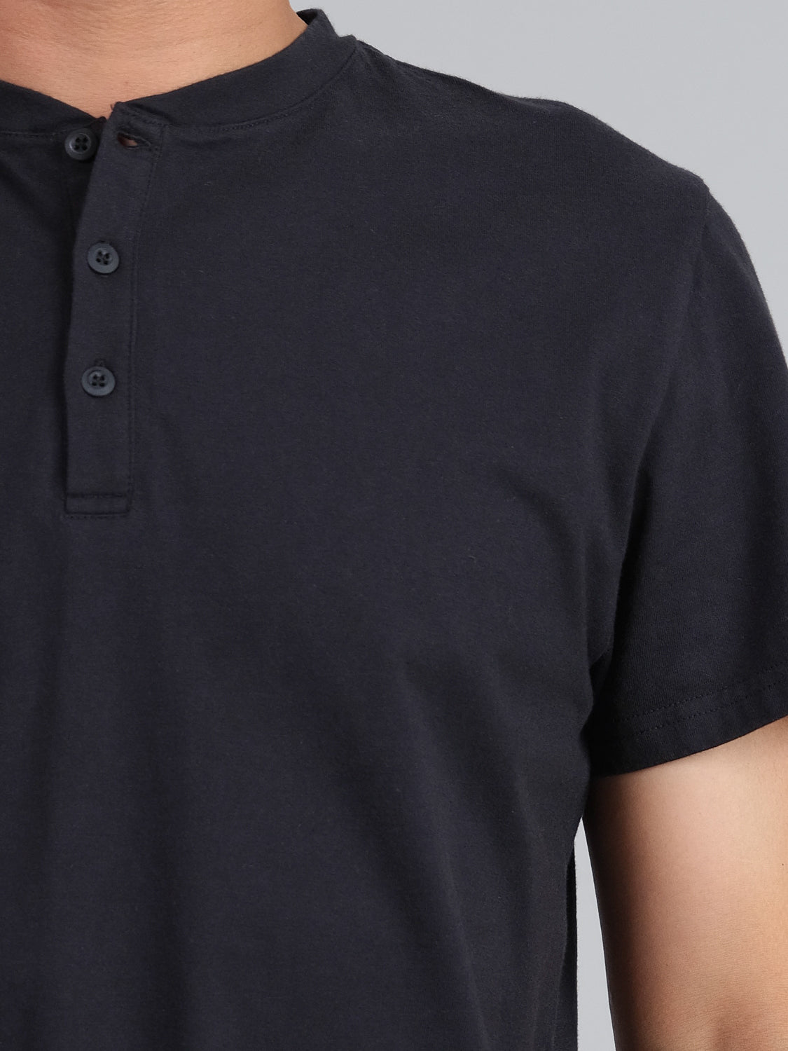 The image shows someone in a chic Champion Organic Cotton Henley by ID Menswear. Its dark navy blue tone, short sleeves, and three undone buttons define a classic look against a plain, light gray backdrop. Only the upper body is partially visible.