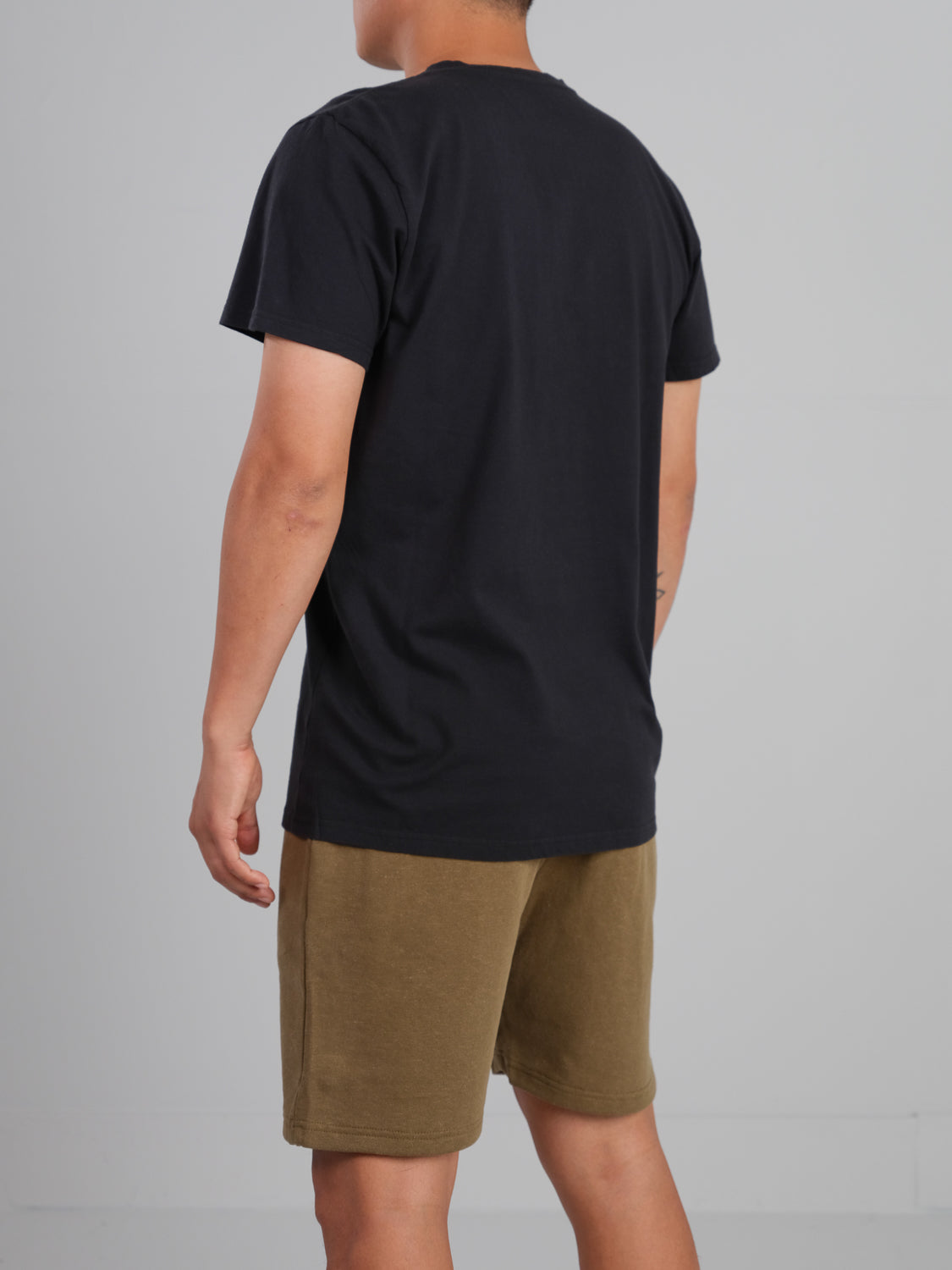 In a light gray room, someone stands out in an ID Menswear Champion Organic Cotton Henley and brown shorts, their classic silhouette highlighted.