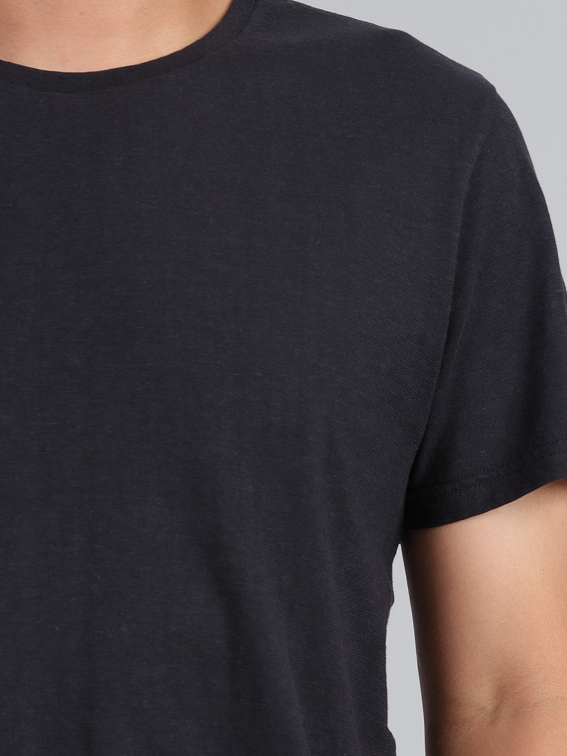 A person is partially visible from the chest up, wearing the ID Menswear Dope Hemp Organic Cotton Tee, a plain black T-shirt with short sleeves and a round neckline, crafted from sustainable fabric, against a light gray background.