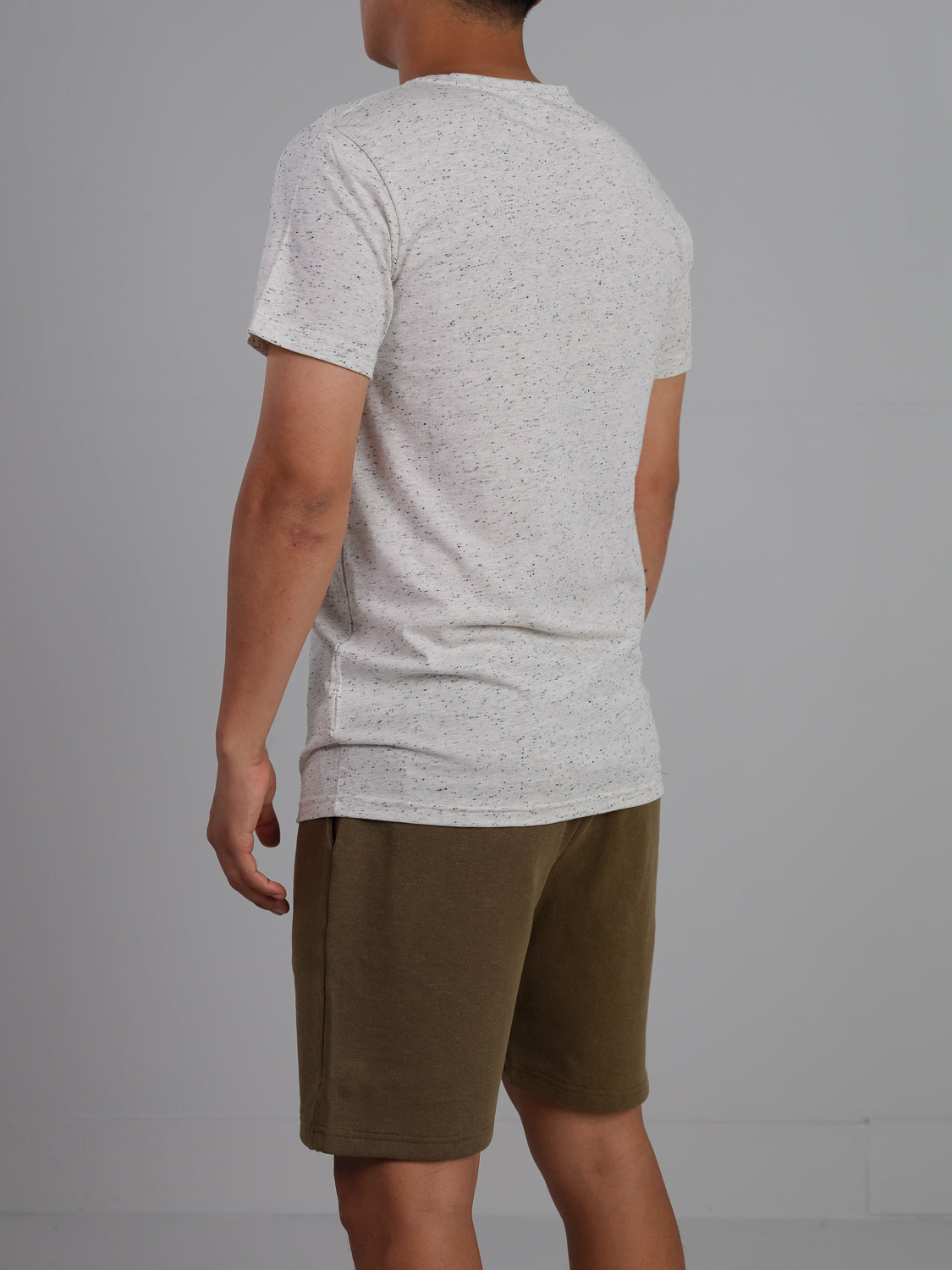 An individual faces away from the camera, modeling an Outclass Speckled Crew Neck Tee by ID Menswear made of soft cotton/poly jersey, paired with green shorts against a plain gray background.