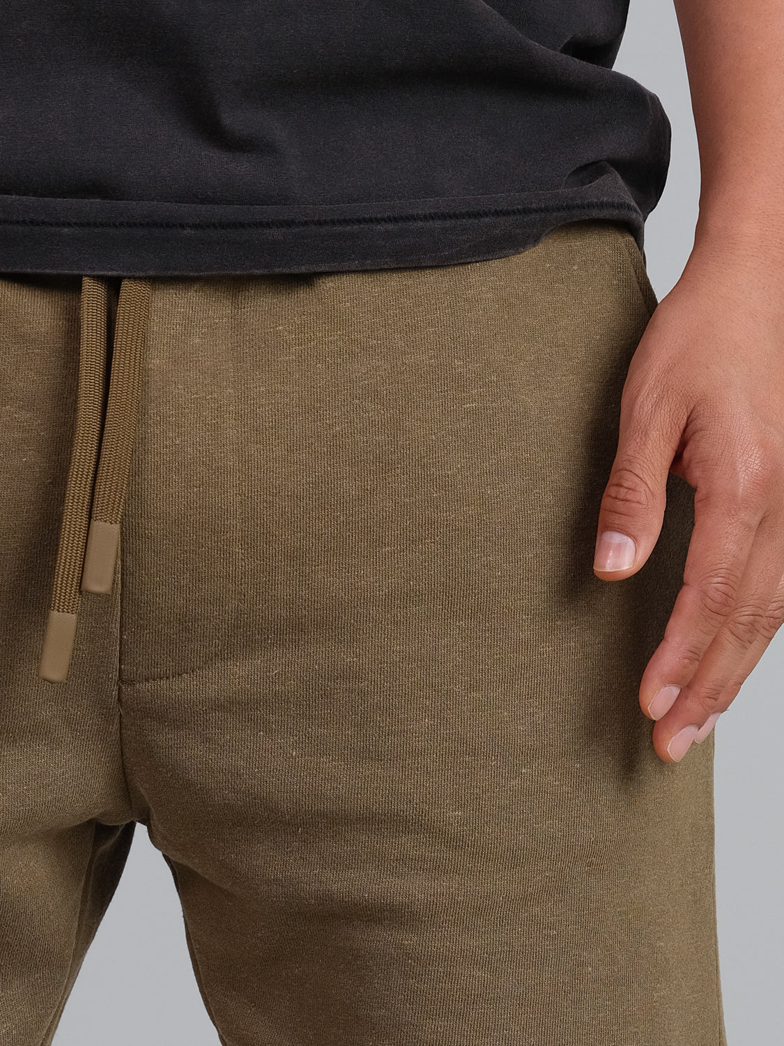 A close-up shows a person wearing an ID Menswear Walker Hemp Cotton Terry Short, featuring relaxed brown drawstring pants. Their left hand is casually by their side, enhancing the laid-back vibe.
