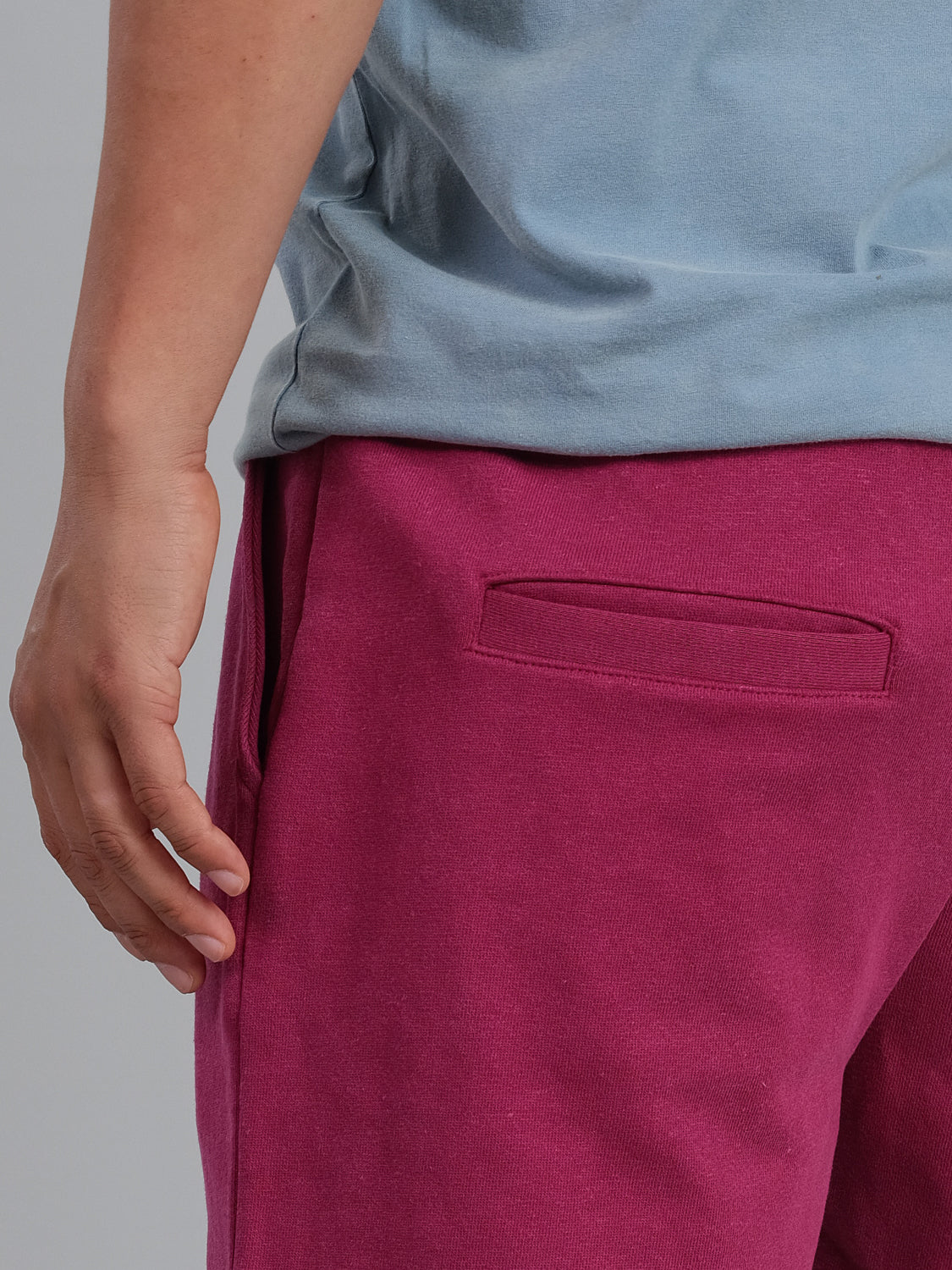 A person is wearing a light blue shirt and Walker Hemp Cotton Terry Shorts by ID Menswear. The focus is on the side view of their torso and upper leg, with their left hand resting by their side and a back pocket on the maroon shorts visible.