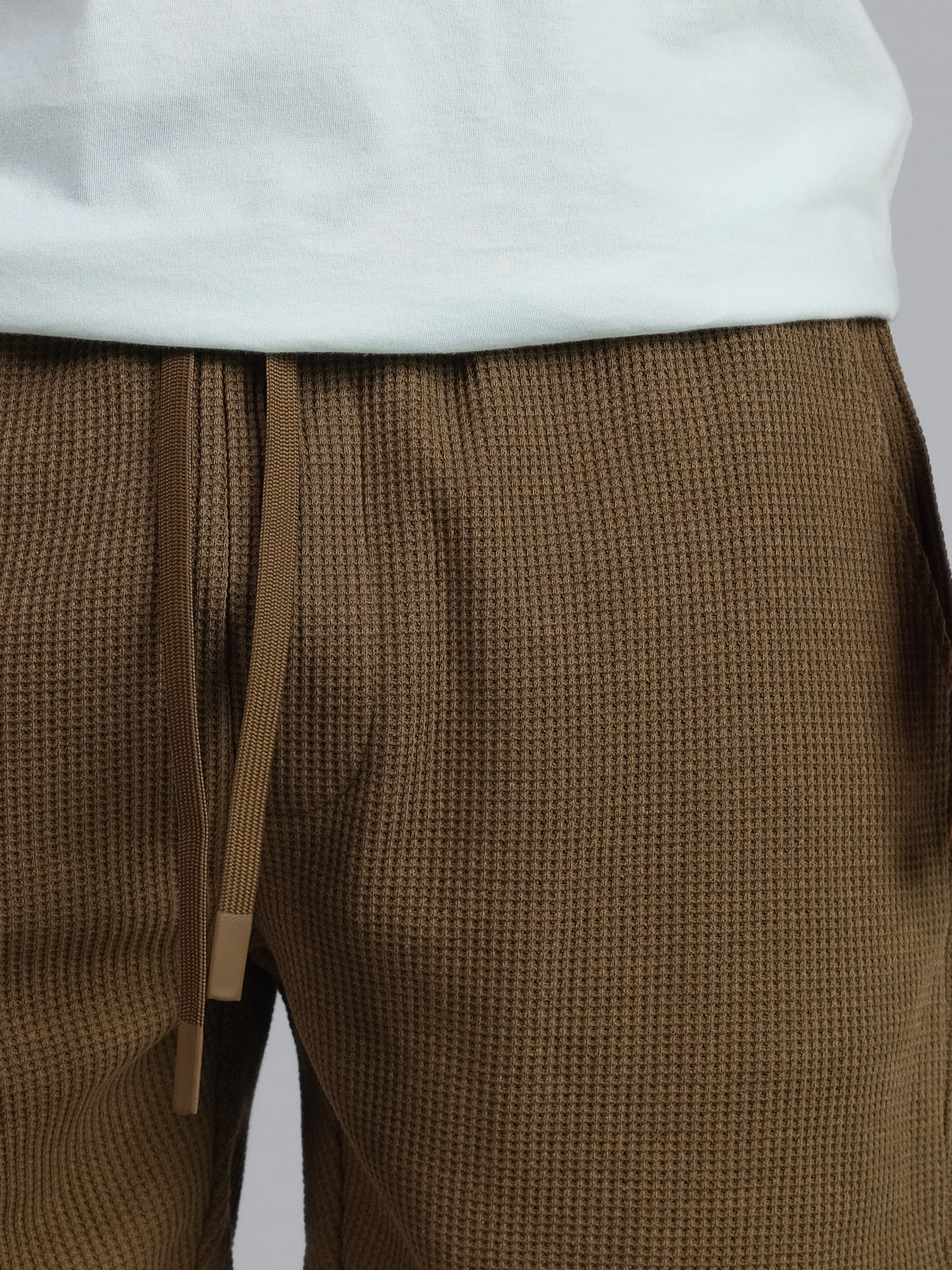 Close-up of someone in a white shirt and the Walker Waffle Knit Short by ID Menswear. The focus is on the brown shorts waffle-knit texture and comfy waistband.