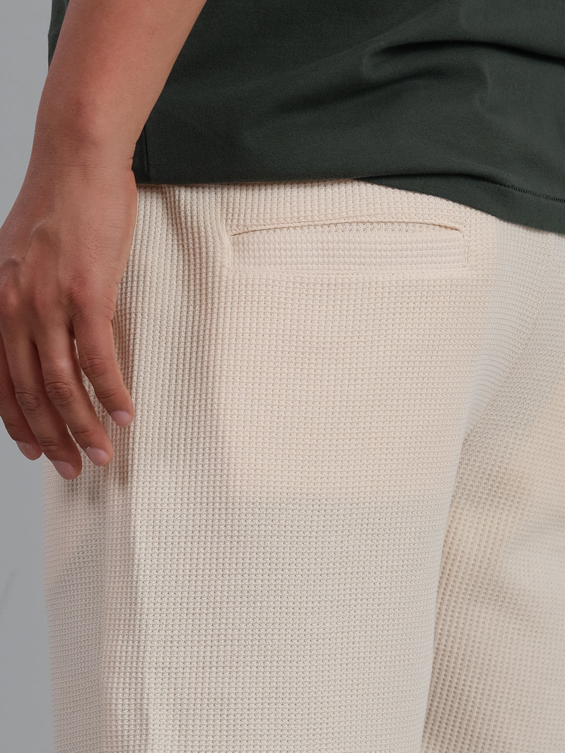 A person wears ID Menswears Walker Waffle Knit Short, showcasing the cream texture and hip pocket detail, paired with a dark green top. Their hand is relaxed at their side.