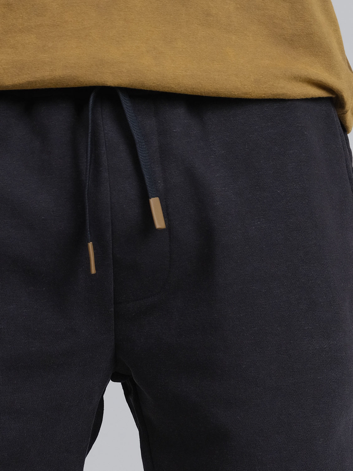 A person wears ID Menswears Walker Hemp Cotton Terry Short, featuring a natural waist design and drawstring with metal tips, paired with a brown shirt.