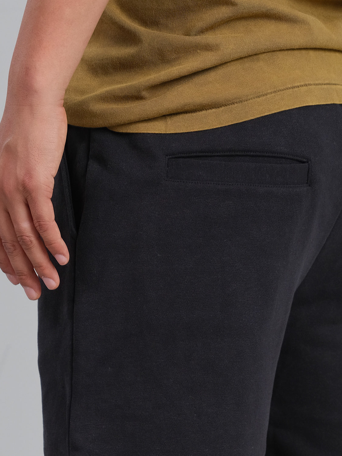 A person is seen in a mustard yellow shirt and Walker Hemp Cotton Terry Short by ID Menswear. Visible from the lower torso, their hand rests casually, and the shorts back pocket seam adds style to the relaxed look.