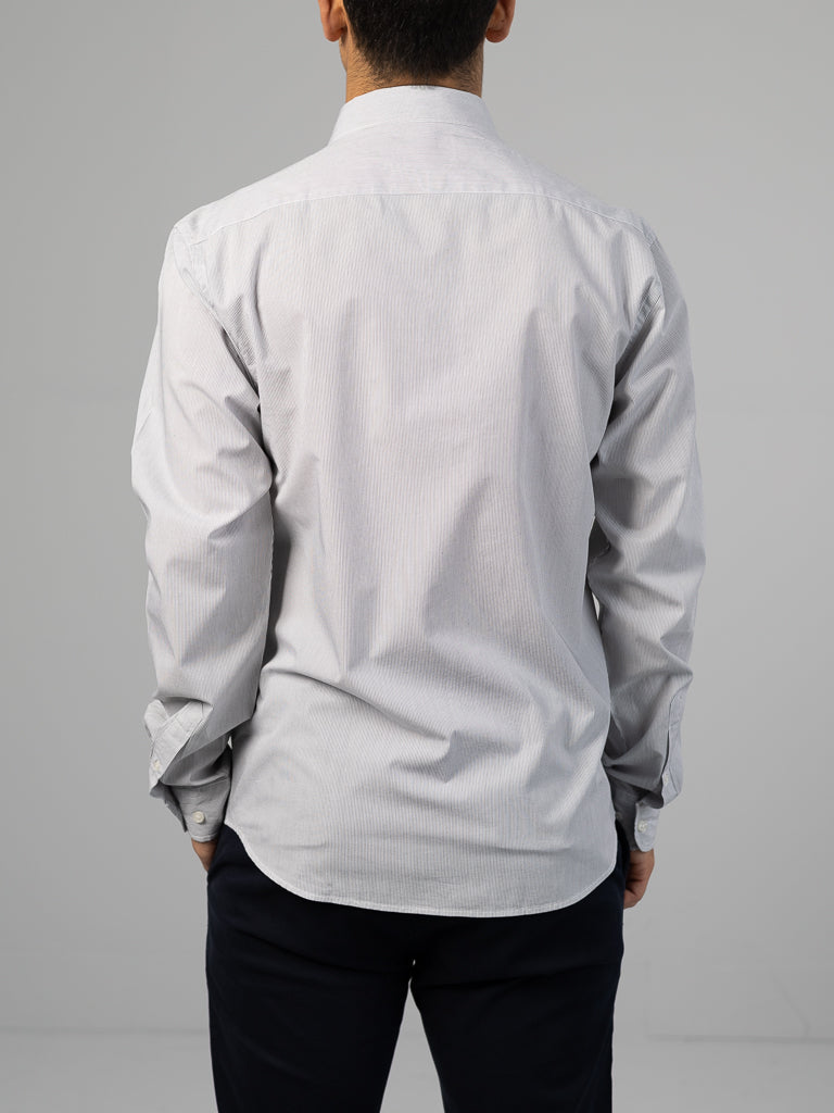 A person facing away from the camera wears the Wade Stripe Button Down Shirt by ID Menswear. This light-colored, regular-fit, long-sleeve shirt features subtle stripes, paired with dark pants against a plain gray background highlighting its understated 100% cotton elegance.