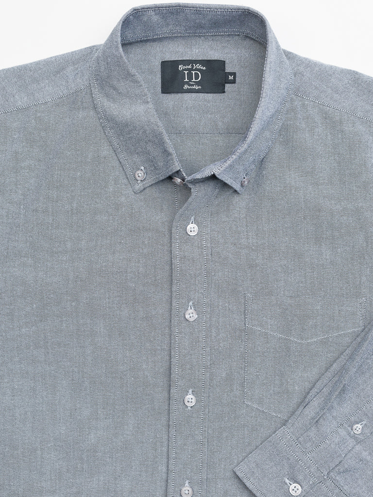 This grey Oxford Long Sleeve Button Down Shirt by ID Menswear is made from 100% cotton. It features a pointed collar, white buttons, and a left chest pocket. The Good Vibes ID label indicates its regular-fit in medium size.