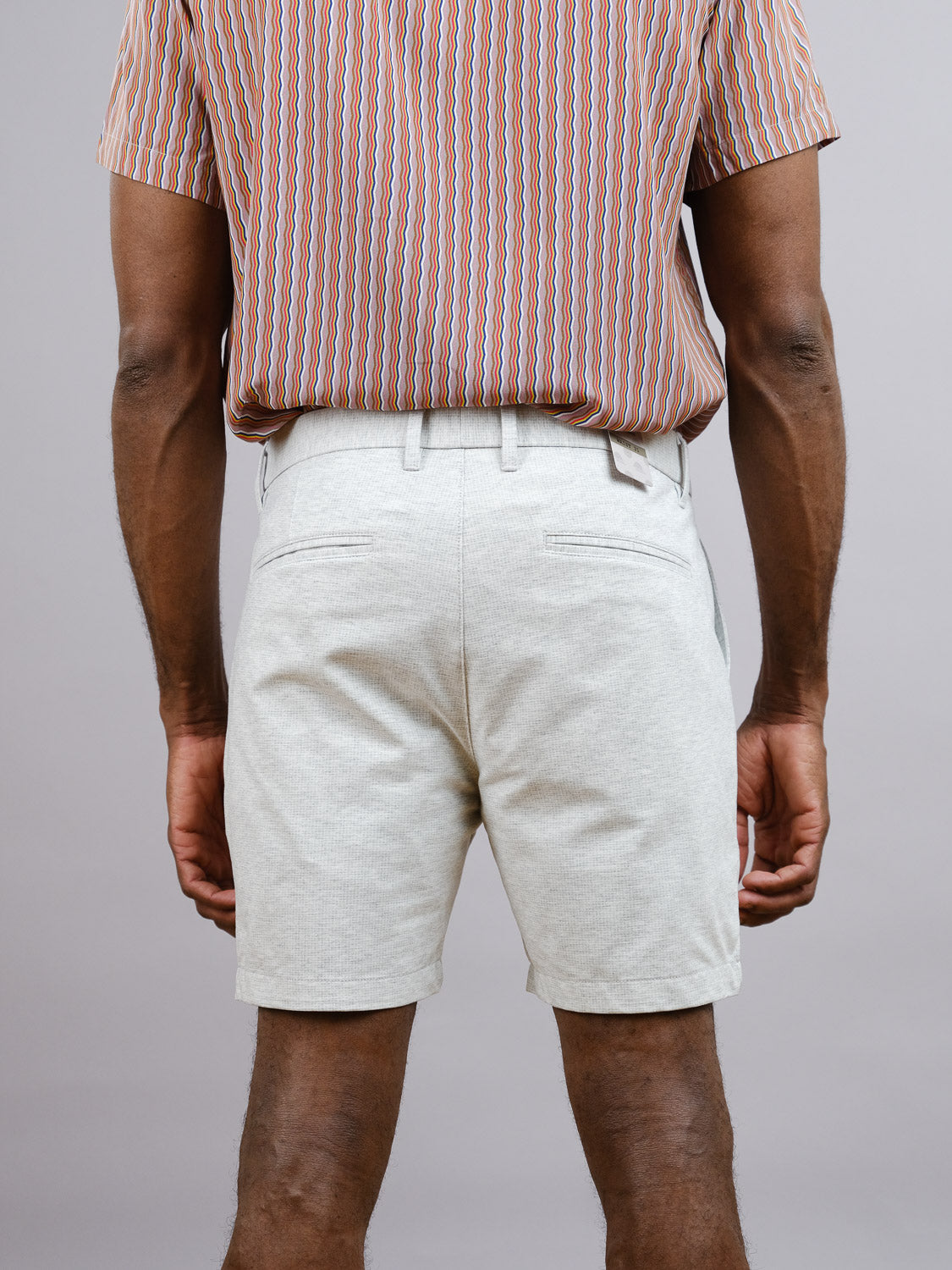 A person faces away from the camera in a striped short-sleeve shirt tucked into ID Menswear’s Eckford 5 Inseam Stretch Short, providing all-day comfort against a plain background.