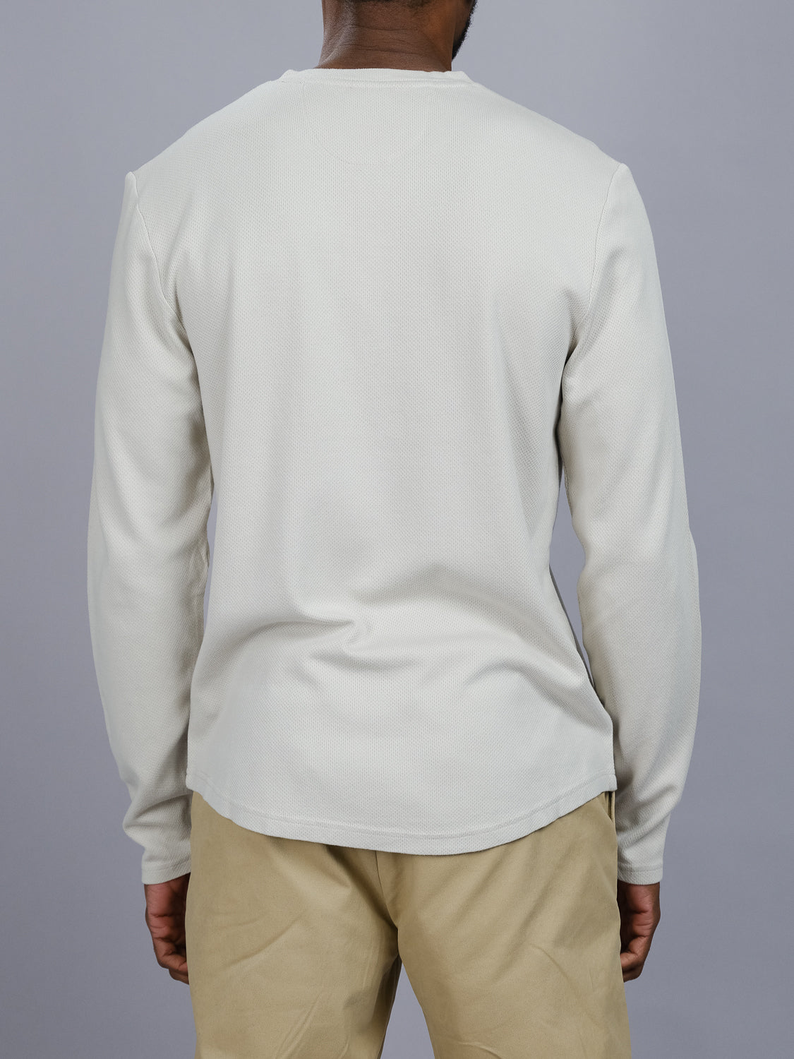 A person is seen from the back in a light gray Freestyle Honeycomb Knitted Mesh Henley from ID Menswear, paired with beige pants, against a solid gray background. The Henley is simple and pattern-free.