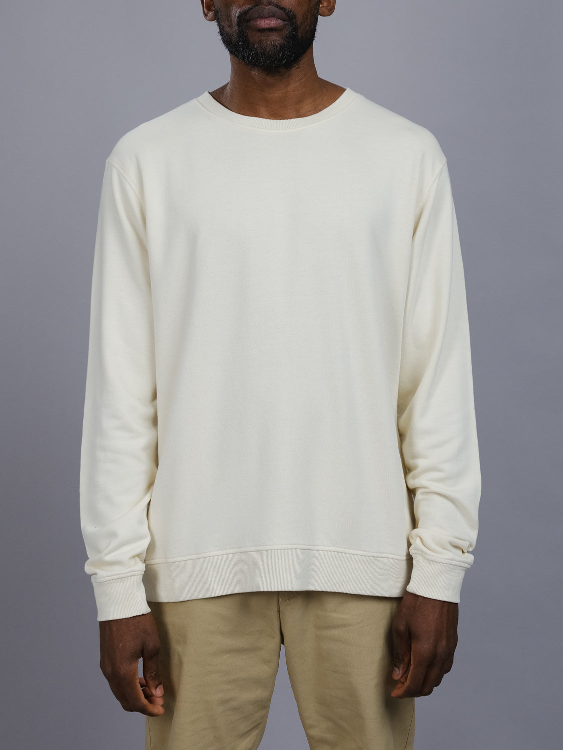 A man in a Champ Bamboo Organic Cotton Sweatshirt from ID Menswear and khaki pants stands against a gray background, his arms relaxed by his sides, exuding effortless style.