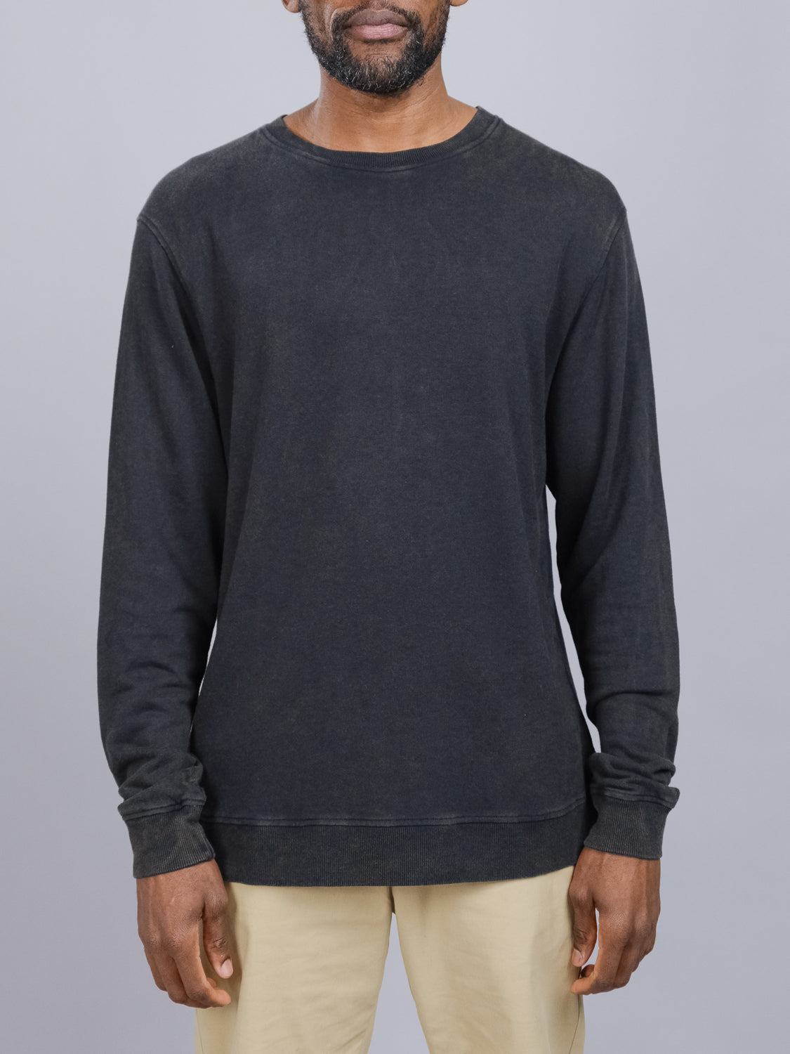 A person is wearing the Champ Bamboo Organic Cotton Sweatshirt by ID Menswear, a plain black long-sleeve made from soft organic cotton, paired with beige pants, standing against a gray background with their face not visible.