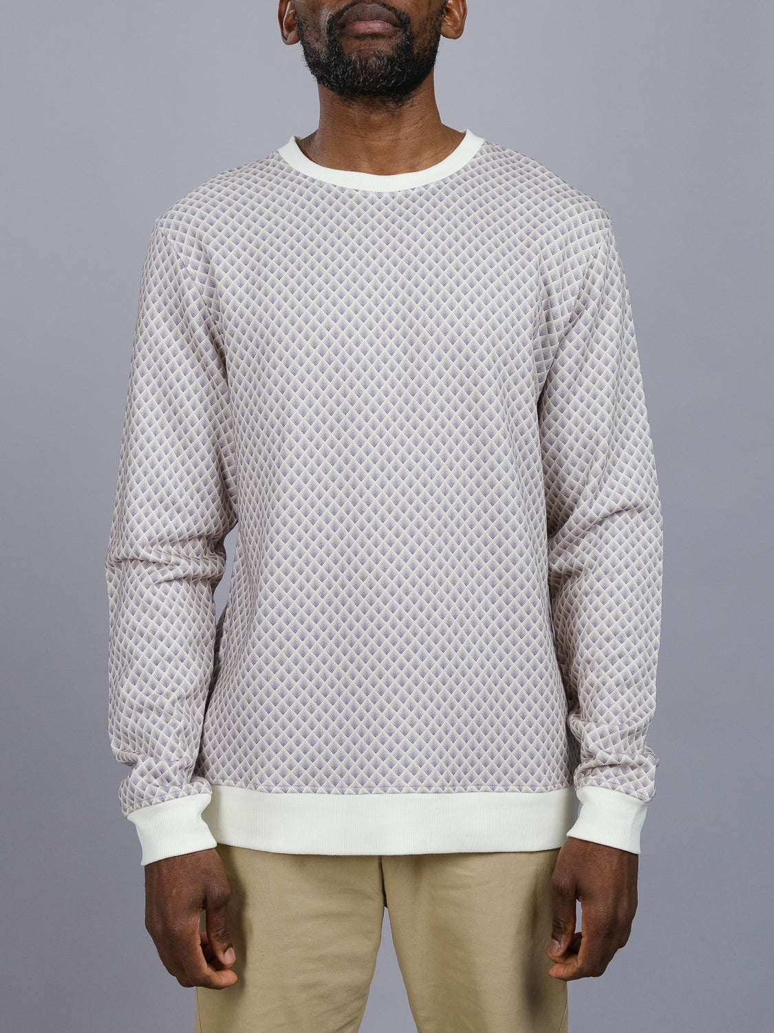 A person in an ID Menswear Carp Geometric Printed Sweatshirt featuring a light-hued pattern with cream cuffs and collar stands against a gray background. Made from bamboo and organic cotton fleece, it pairs effortlessly with their beige pants, while their hidden face adds a modern artistic touch.