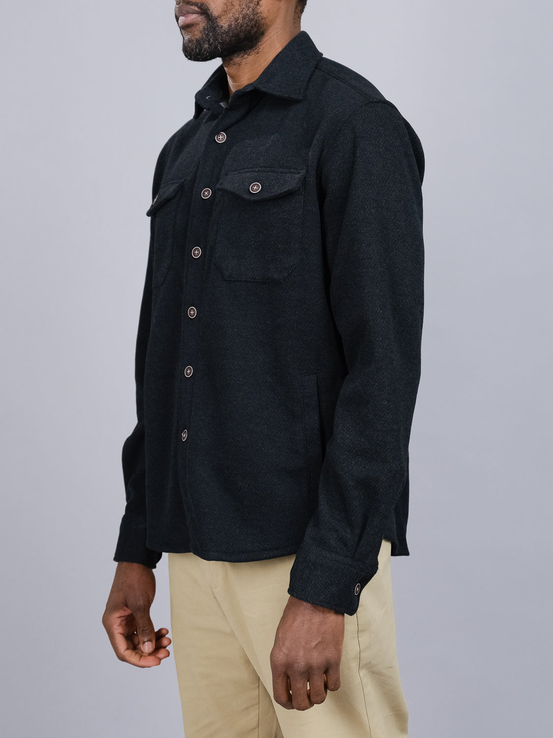 A person models an ID Menswear Yukon Shirt Jacket with two chest pockets against a gray background. The textured fabric suits transitional weather, pairing effortlessly with light-colored pants for casual outings. Their face is not visible.