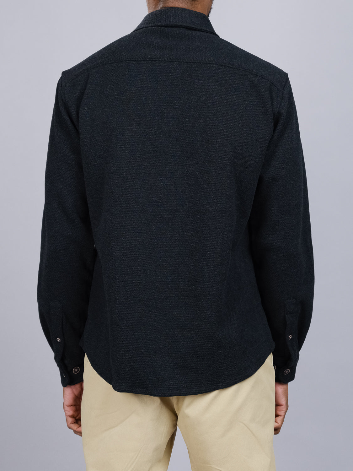 A person in an ID Menswear Yukon Shirt Jacket and light-colored pants stands with their back to the camera, ideal for transitional weather, against a plain gray backdrop.