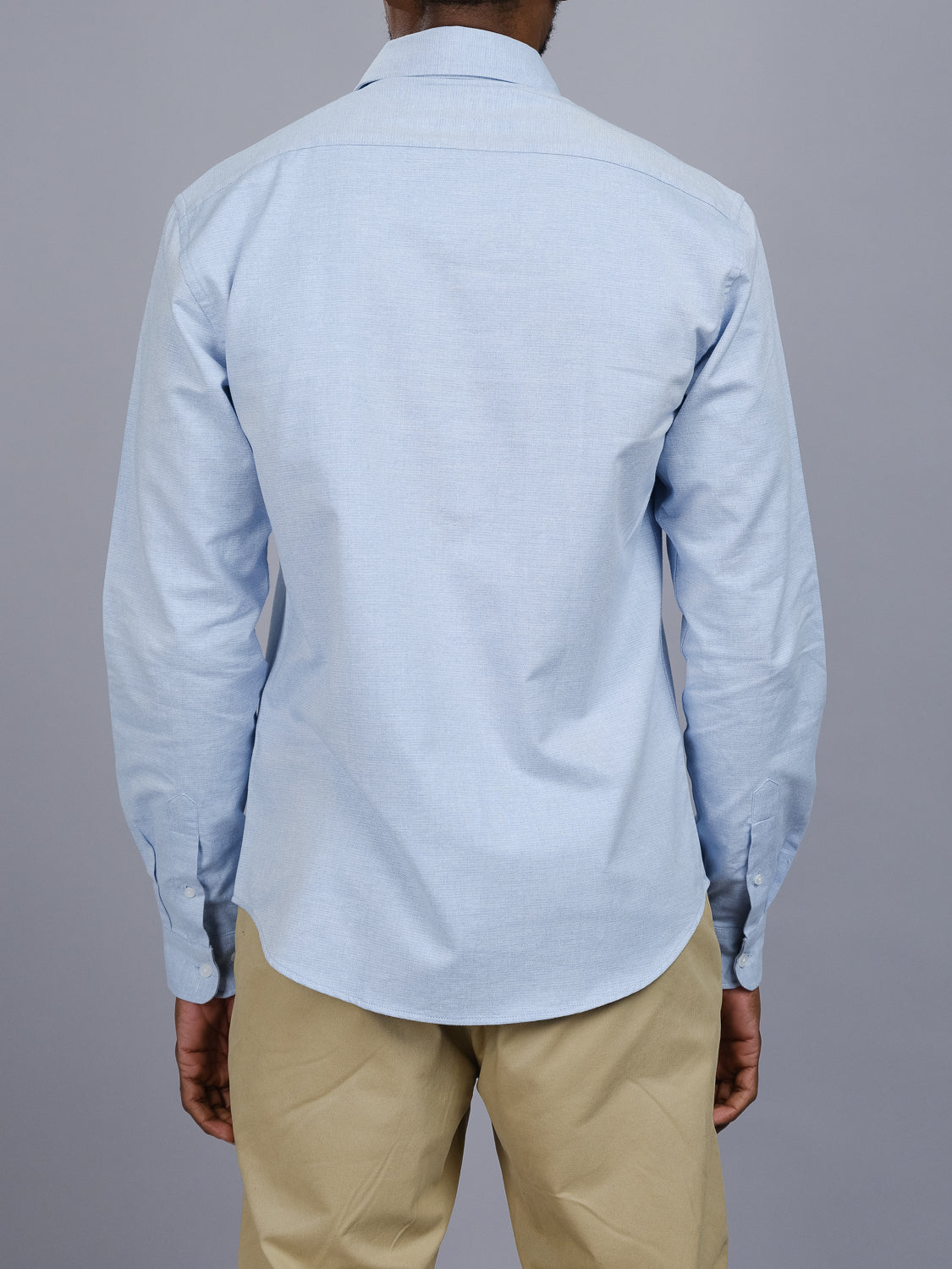 A person wearing the Akira Cotton Button Down Shirt by ID Menswear in light blue, regular fit, paired with beige pants is seen from behind against a simple gray background.