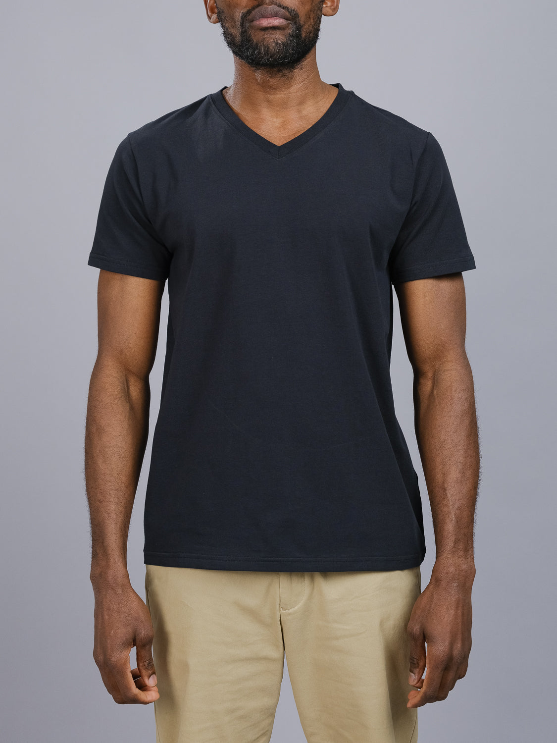 Someone is wearing the ID Menswear Classic V Neck Tee—a wardrobe essential made from a comfortable cotton-spandex blend—along with beige pants, set against a light gray background. The focus is on their upper body with relaxed arms by their sides.