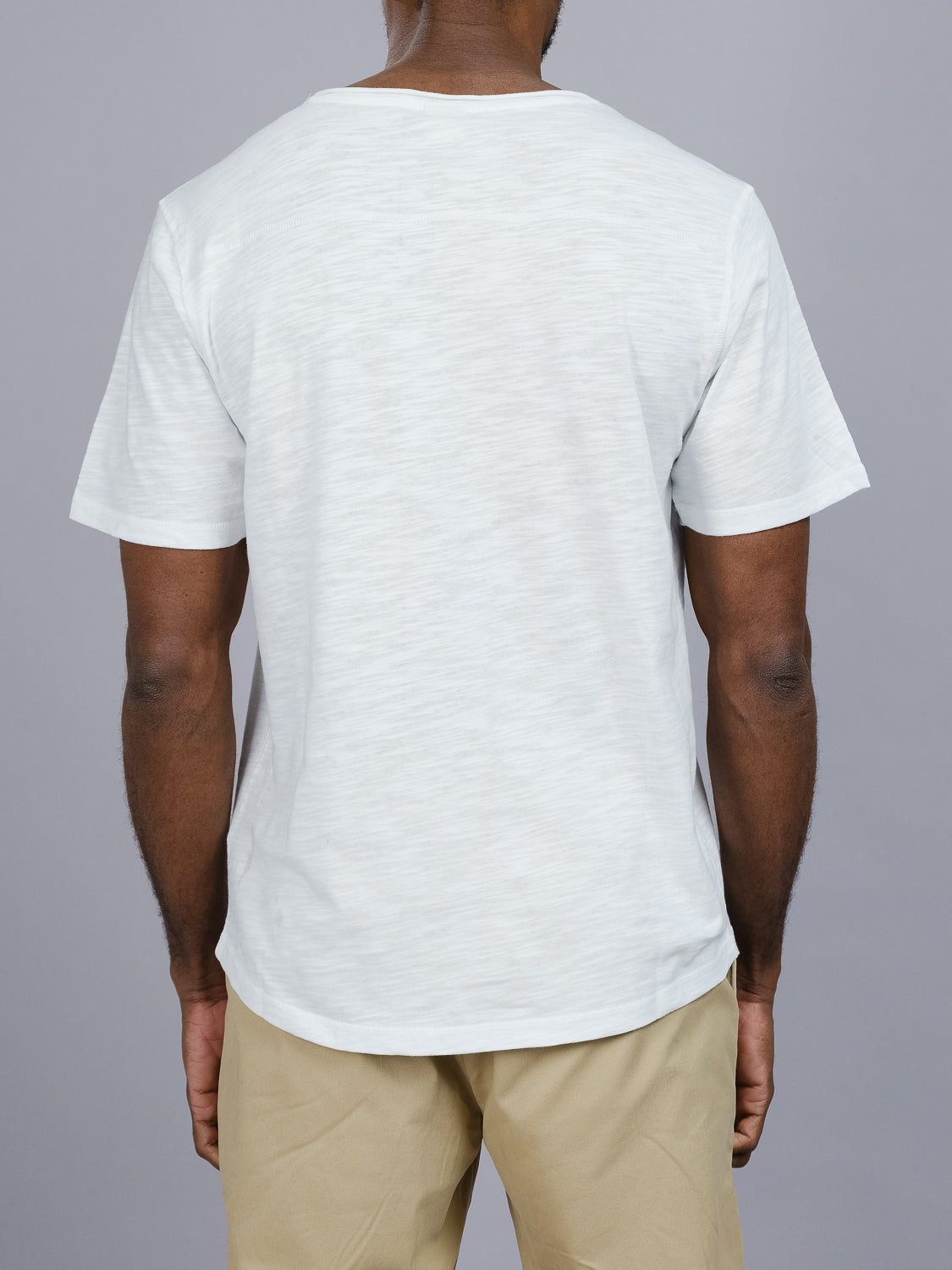 A person is seen from behind wearing an ID Menswear light gray Da Nang Rolled Neck Slub Tee and beige pants against a plain gray background.